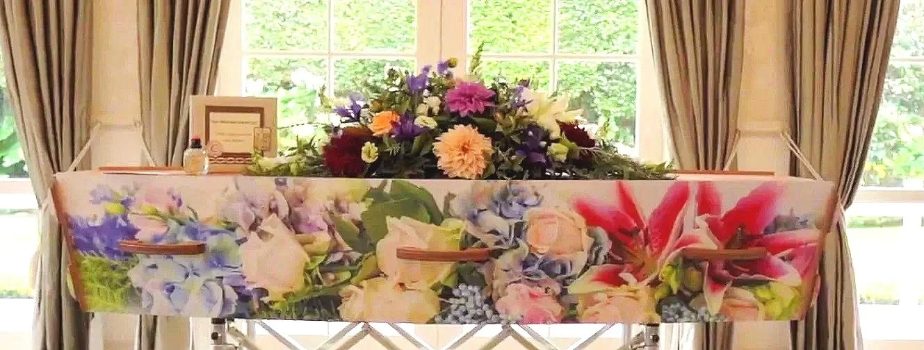 A floral casket with a flower arrangement on top and a bottle of perfume.
