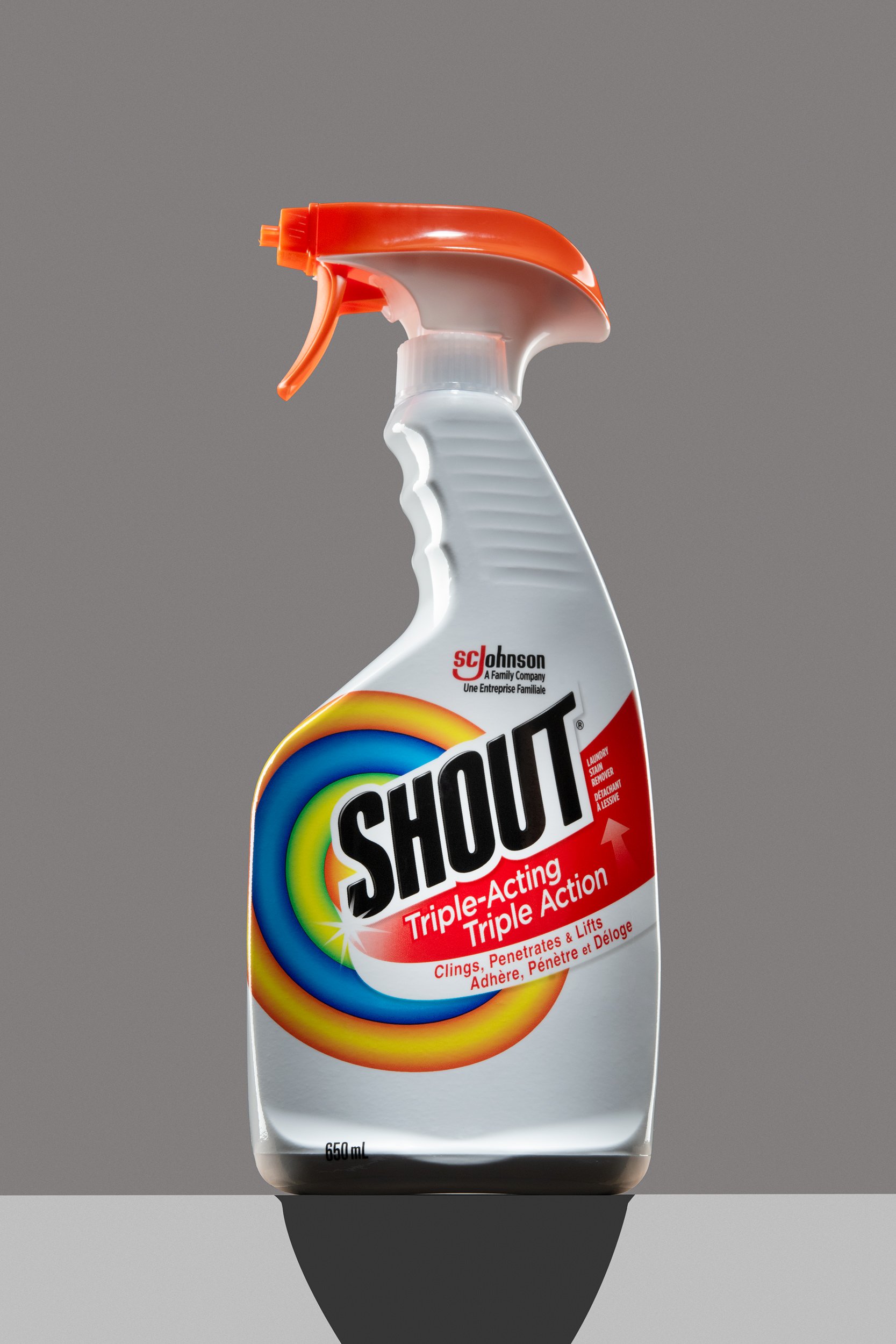 Bottle of Shout Triple-Acting stain remover with orange trigger on neutral grey background