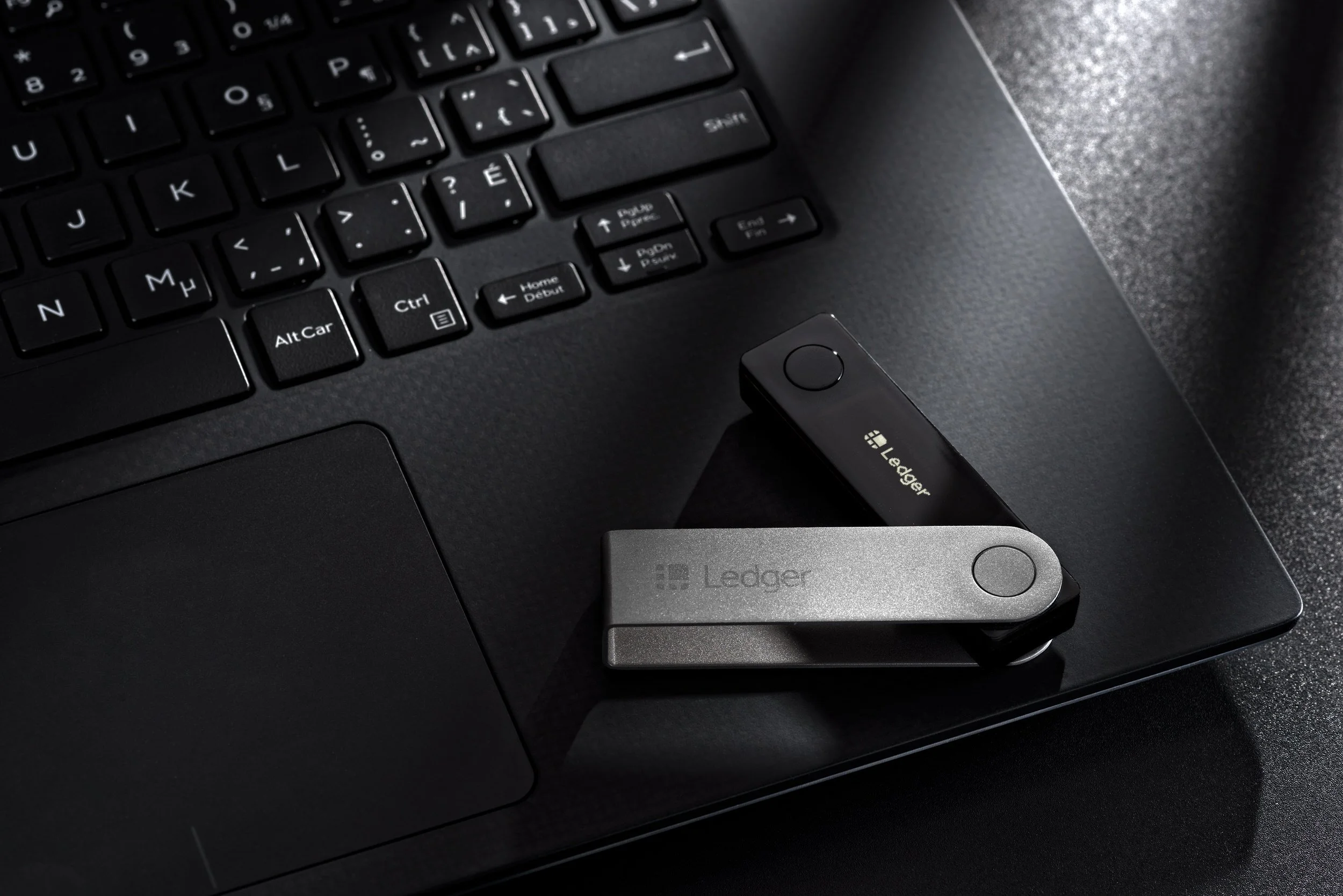 Ledger hardware crypto wallets resting on keyboard and trackpad under soft directional light