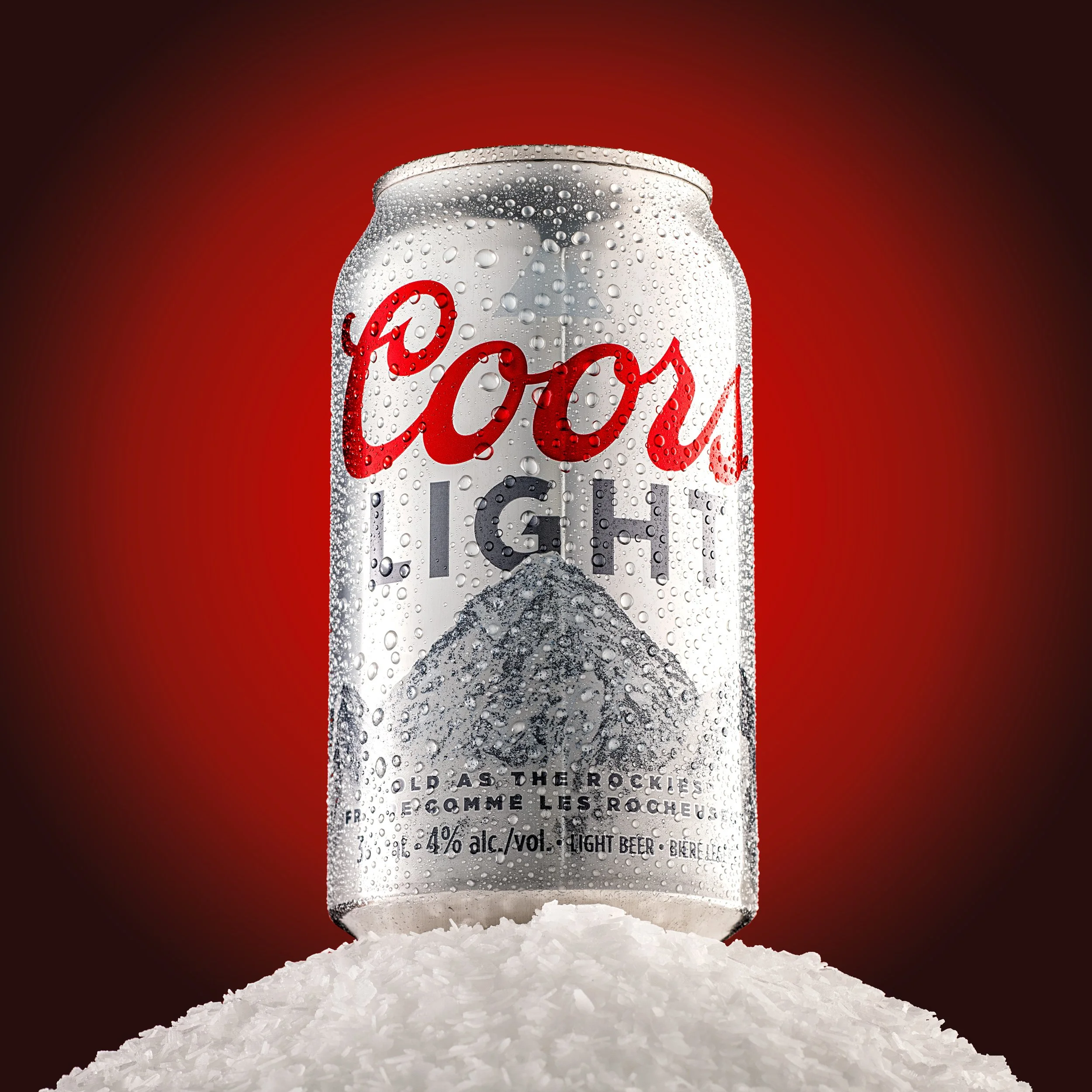 Cold Coors Light beer close-up on a mound of snow on a red backdrop