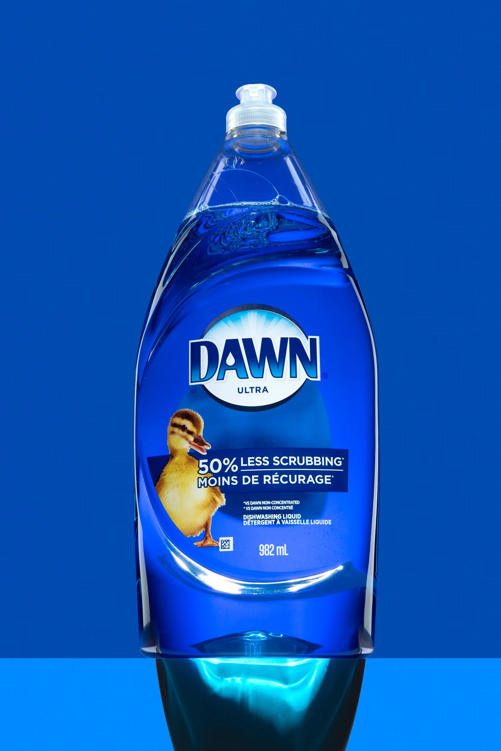 Transparent bottle of Dawn dishwashing liquid with a duckling illustration on bright blue