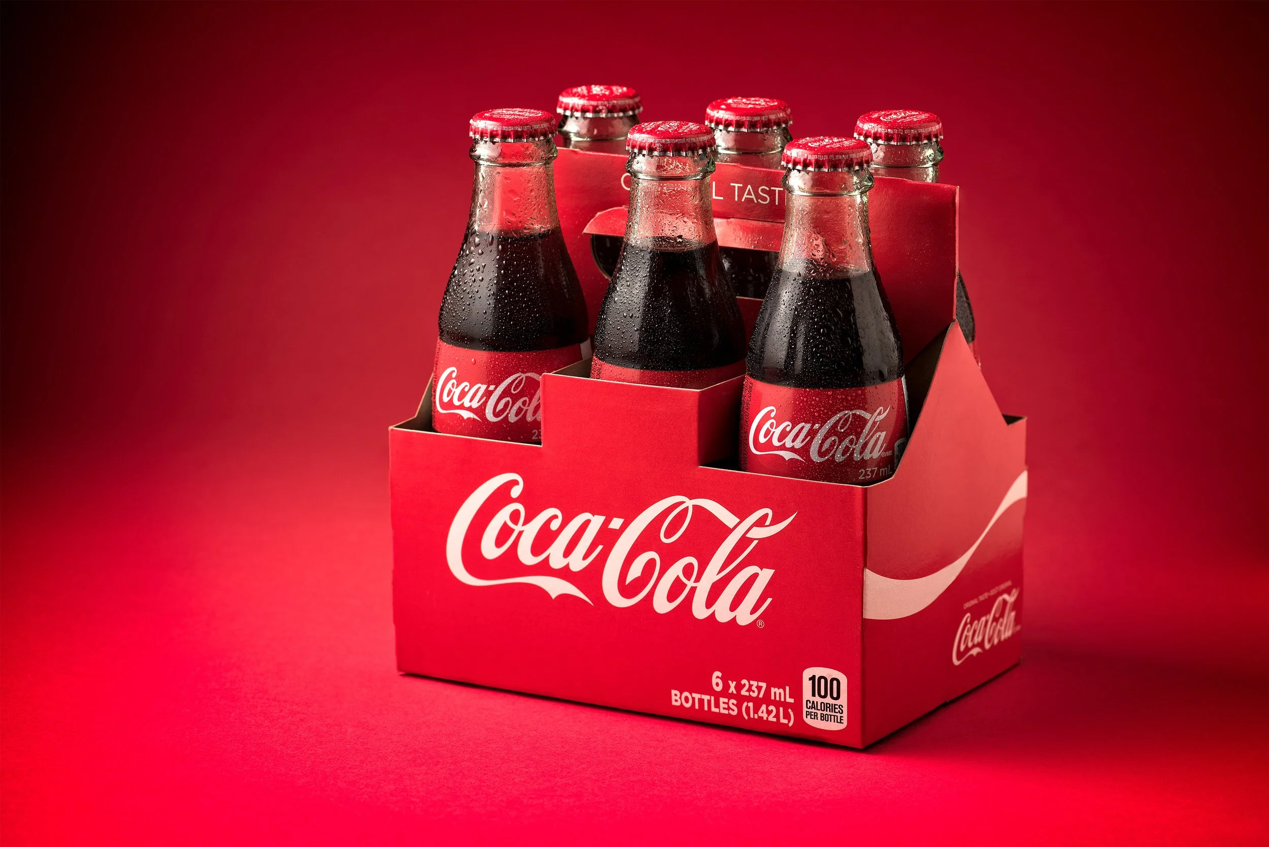 Six pack of CocaCola glass bottles with visible condensation on red background