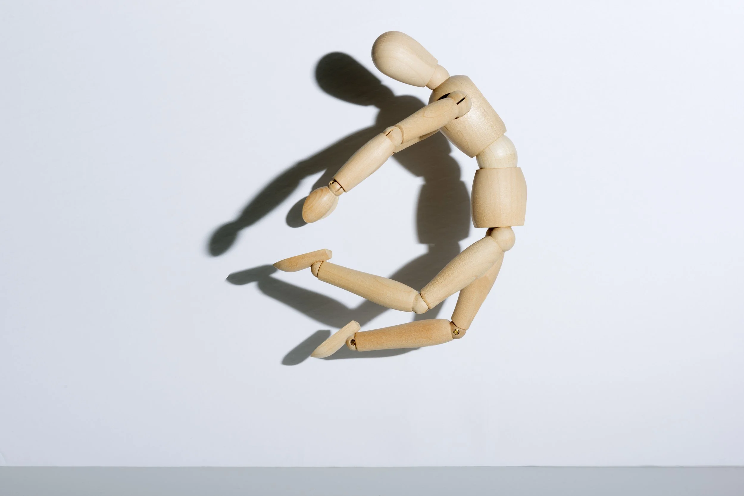 Wood artist mannequin captured midair in crouched jumping motion casting shadow