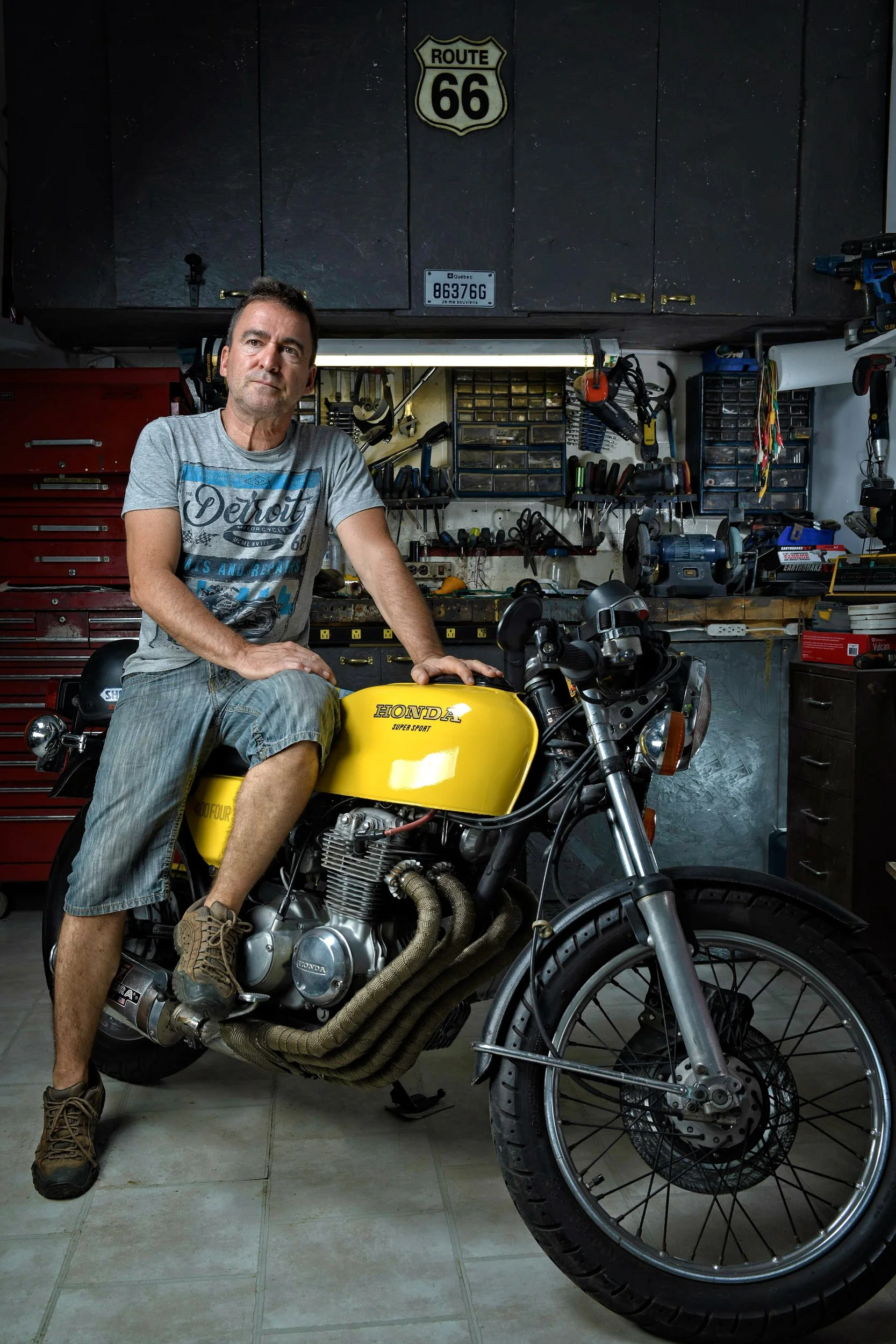 Man sitting on yellow Honda motorcycle in garage workshop with tools and Route 66 sign