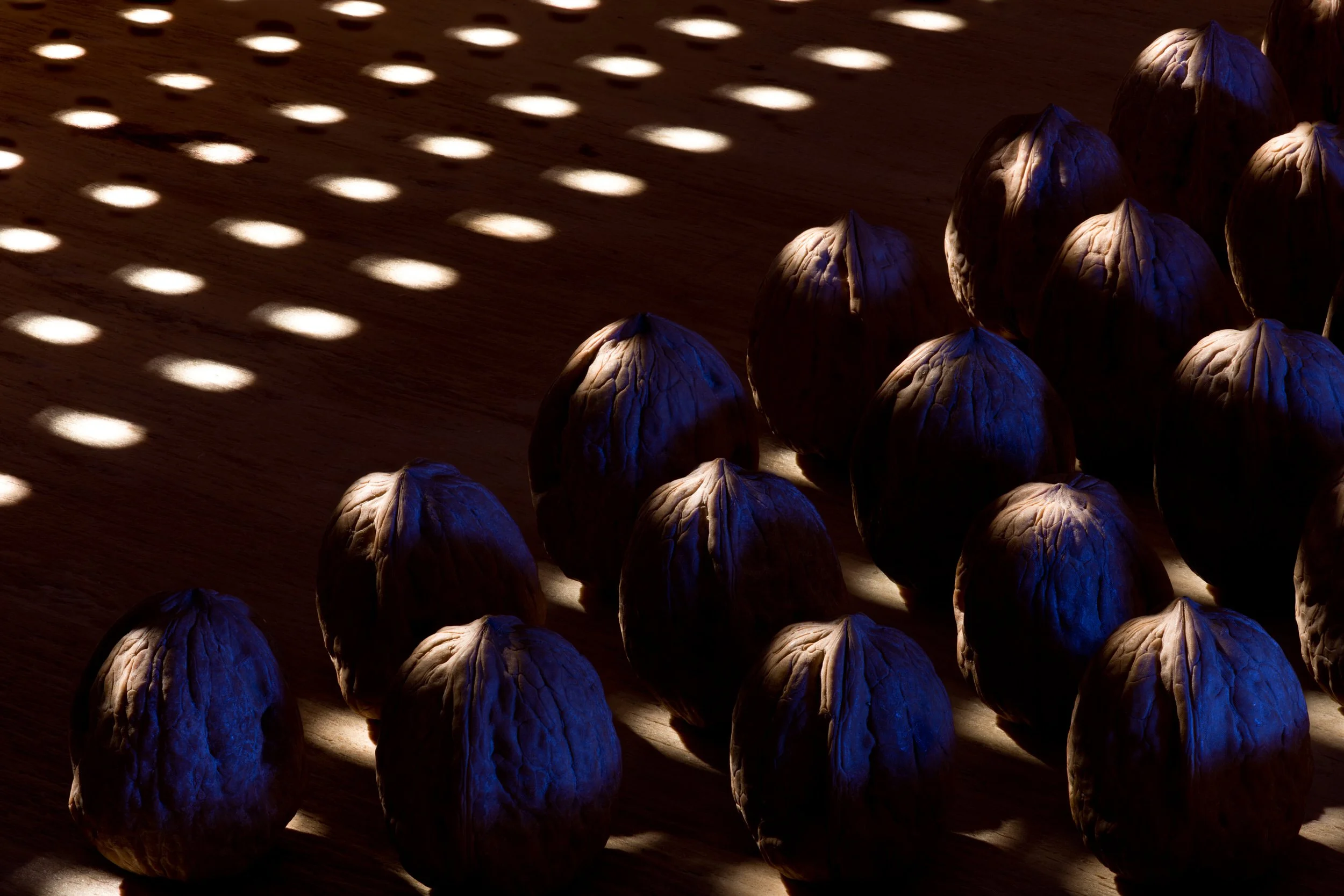 Group of whole walnuts lit by a grid of spotlight patterns casting dramatic shadows
