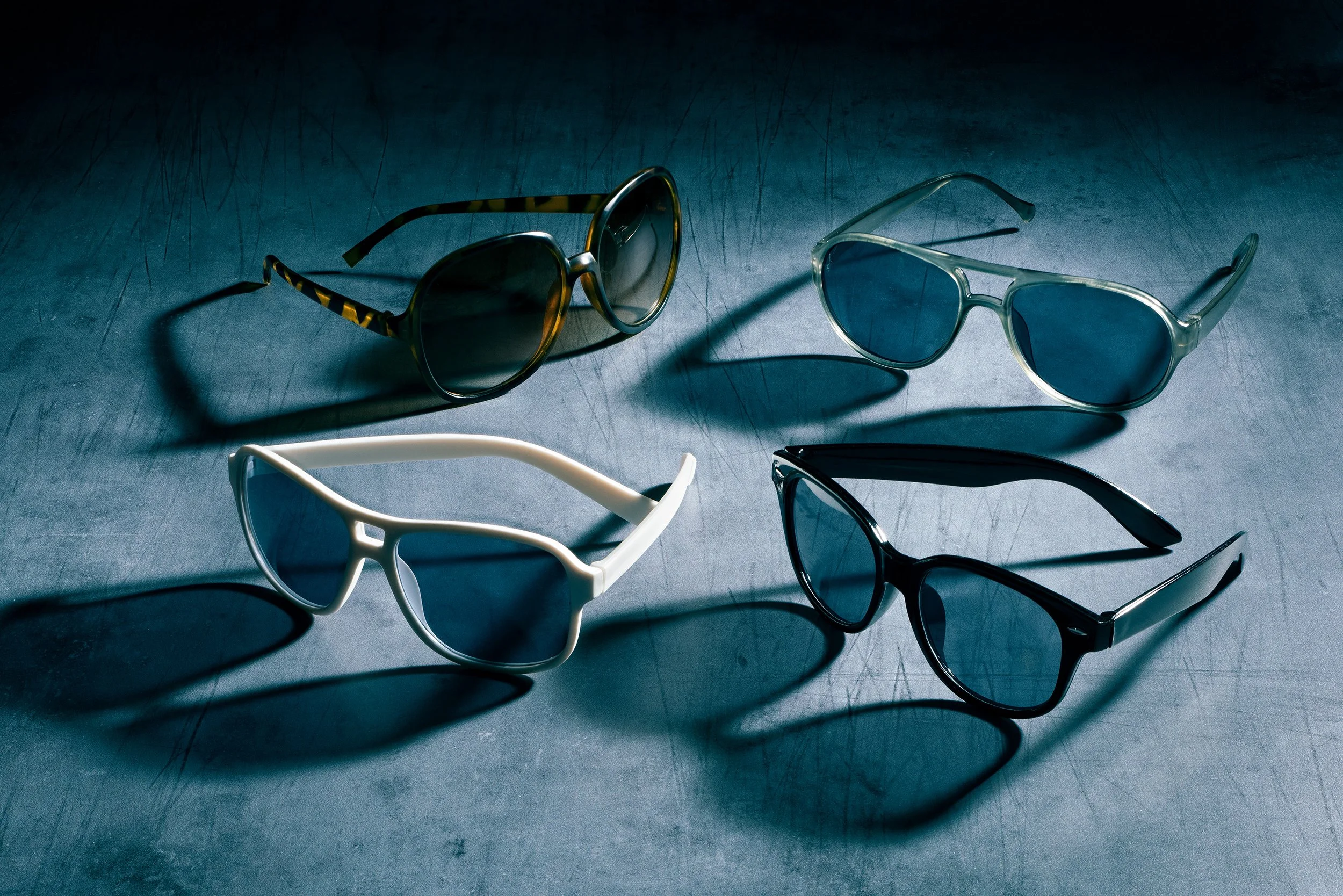 Studio shot of four assorted sunglasses with deep shadows on a textured blue background