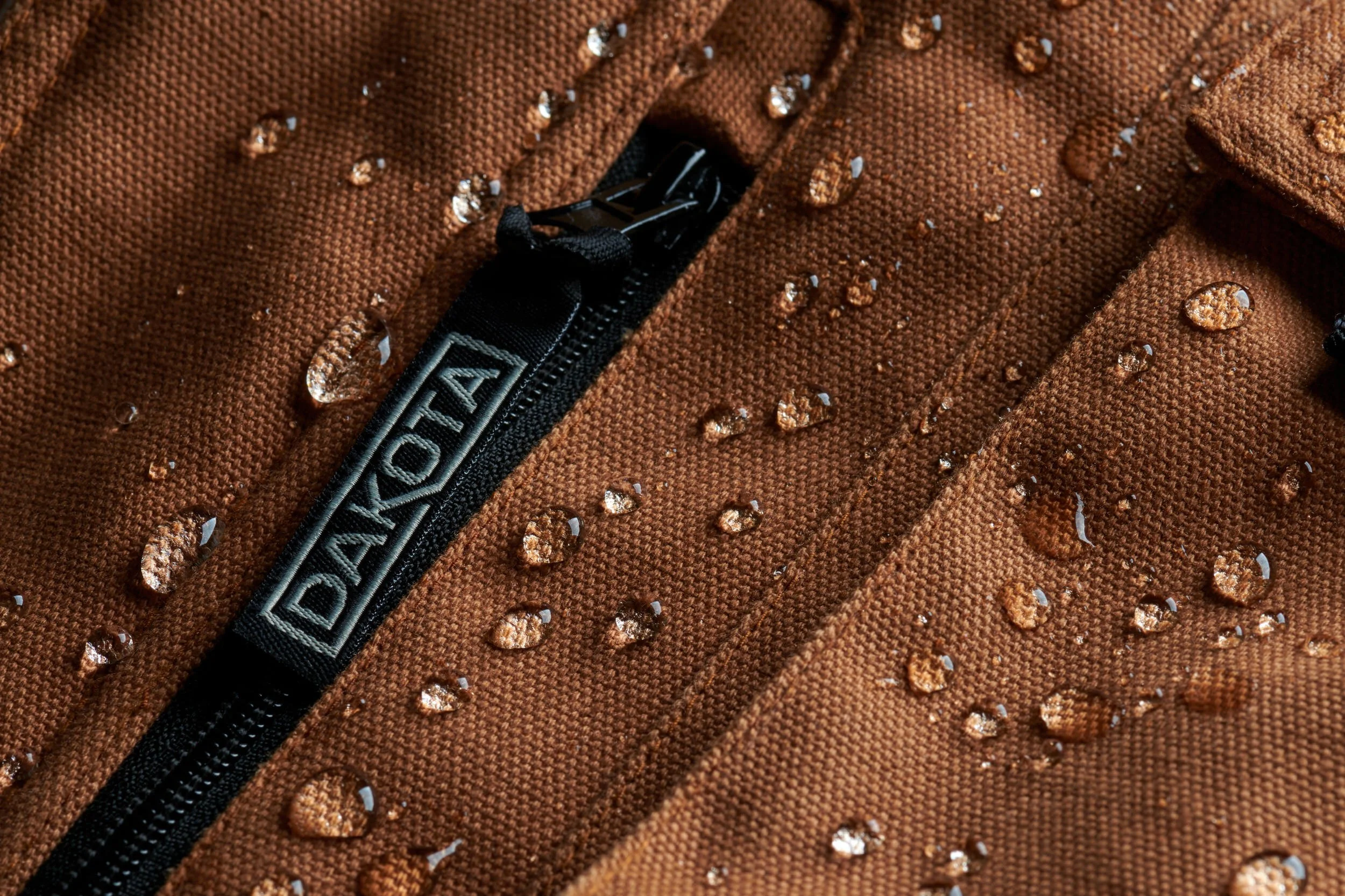 Macro shot of brown textile jacket with visible zipper and water droplets