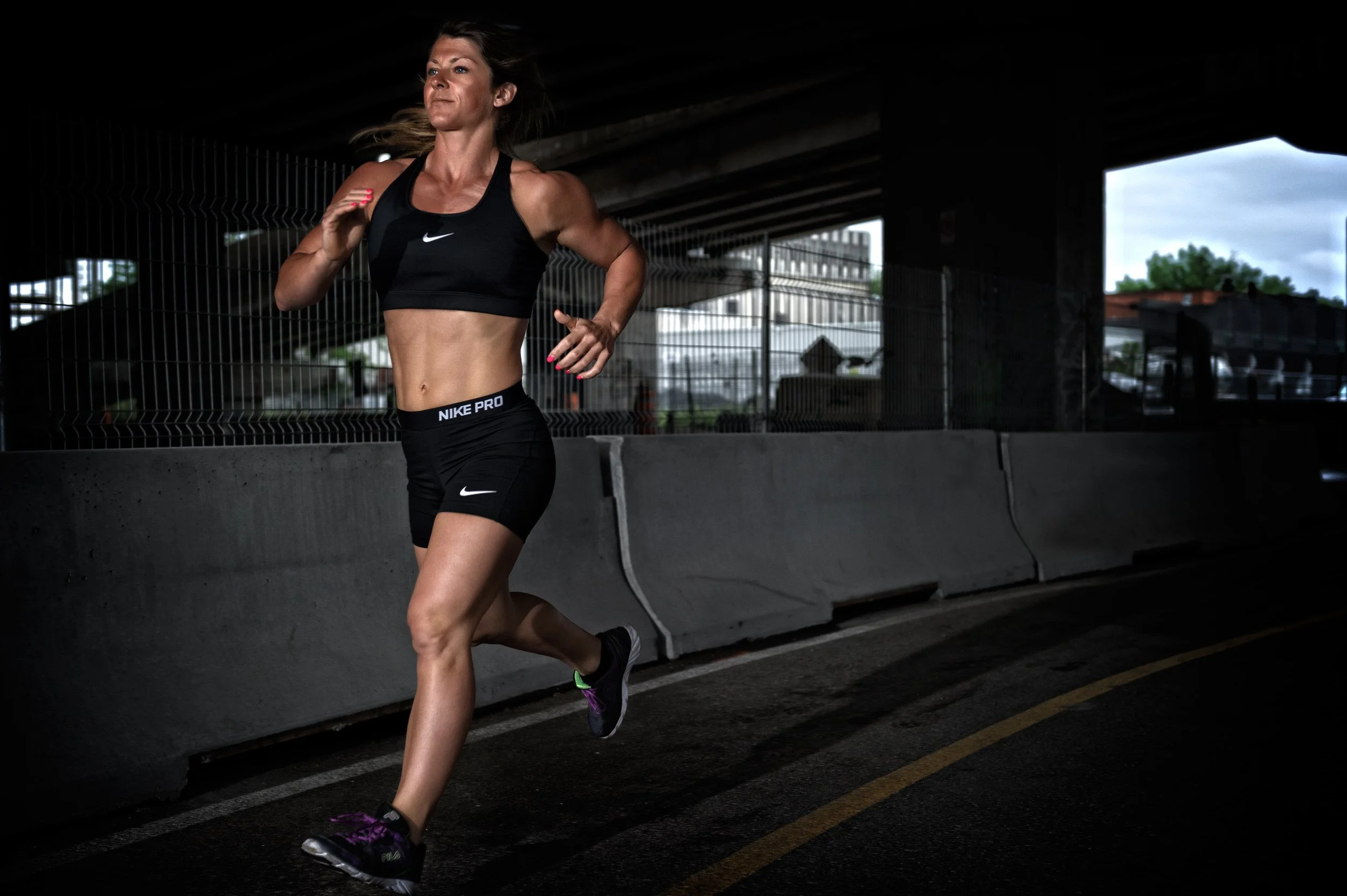 Fit woman mid-stride in sportswear running under a highway bridge