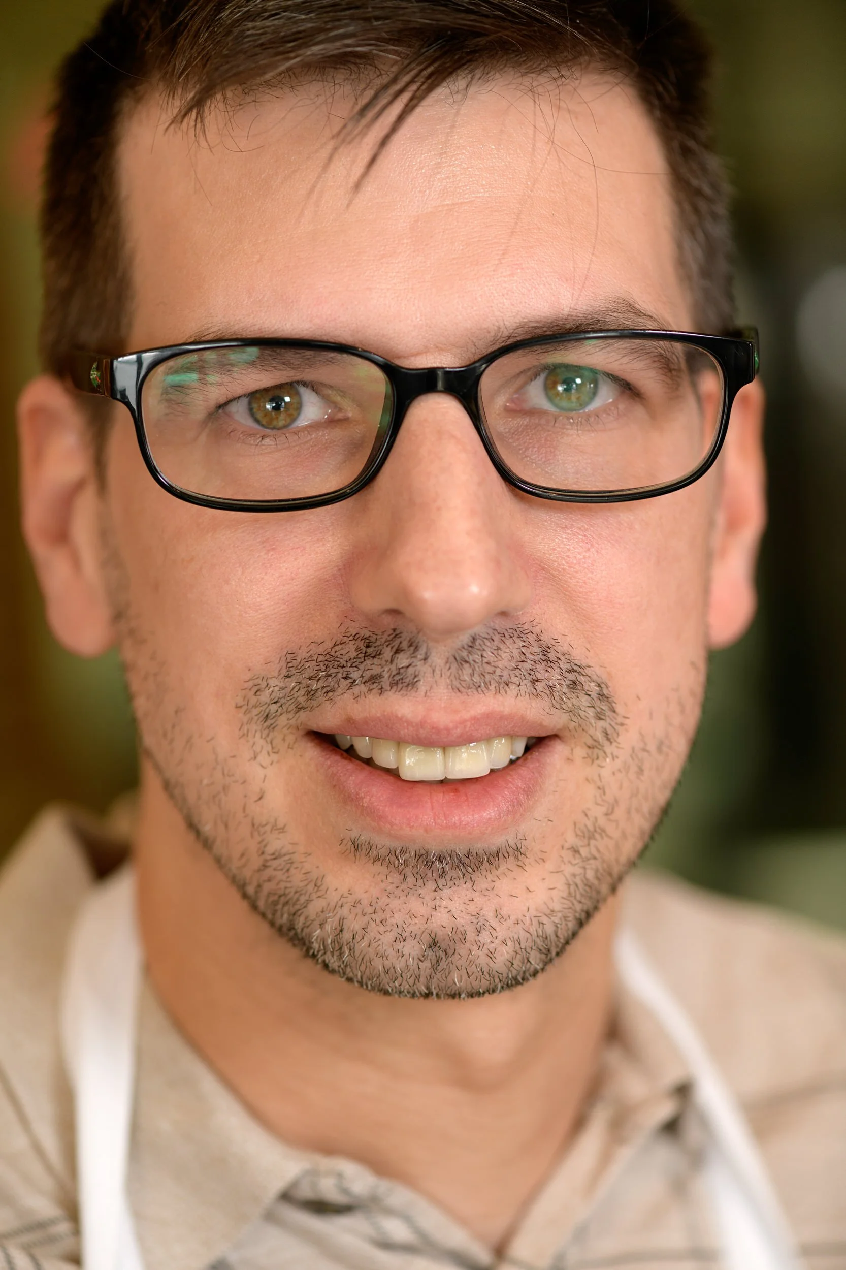Close-up portrait of a smiling male baker with glasses and a short beard wearing a white apron.