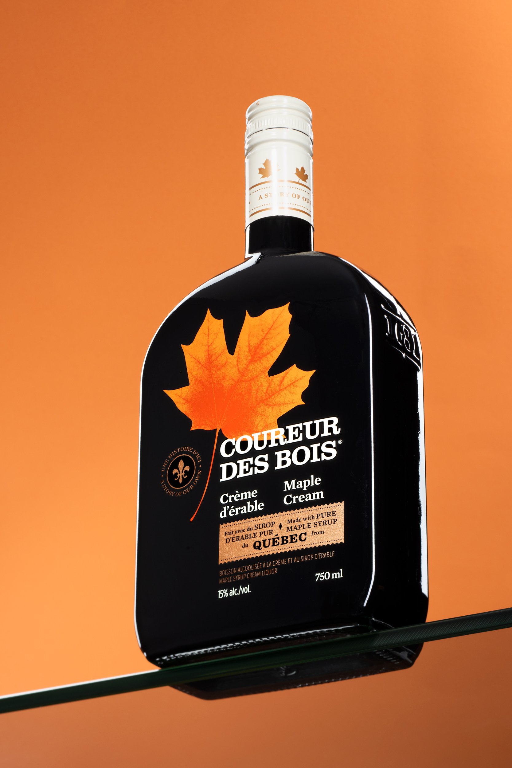 Coureur des Bois maple cream liqueur bottle balanced on a glass shelf at an angle