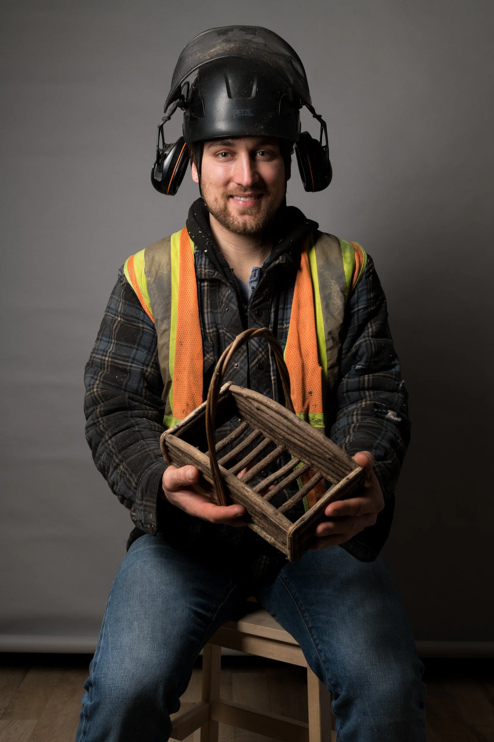 Forestry worker studio portrait wearing helmet and vest holding a wooden basket