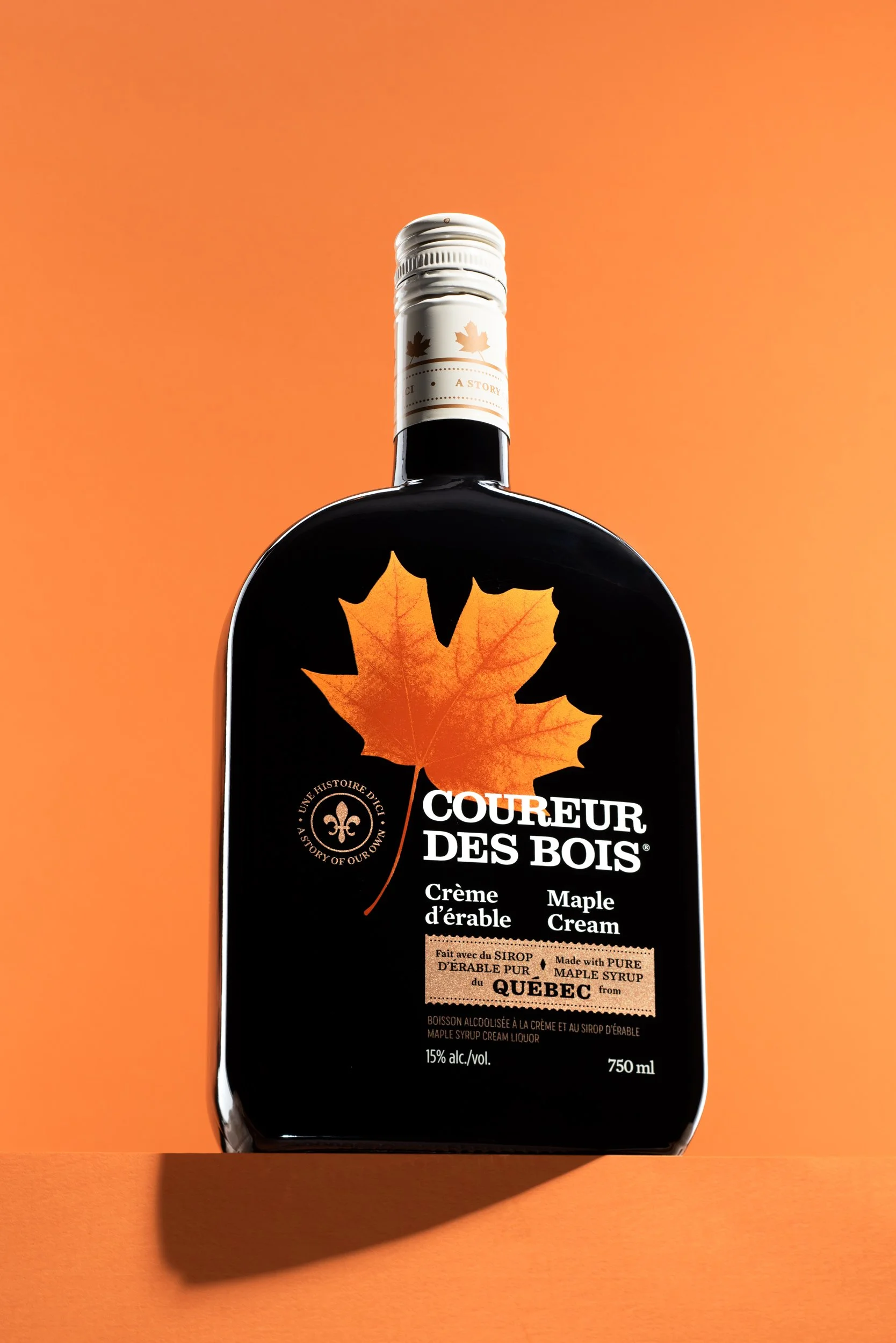 Coureur des Bois maple cream liqueur 750ml bottle on an orange background with a hard cast shadow beneath.