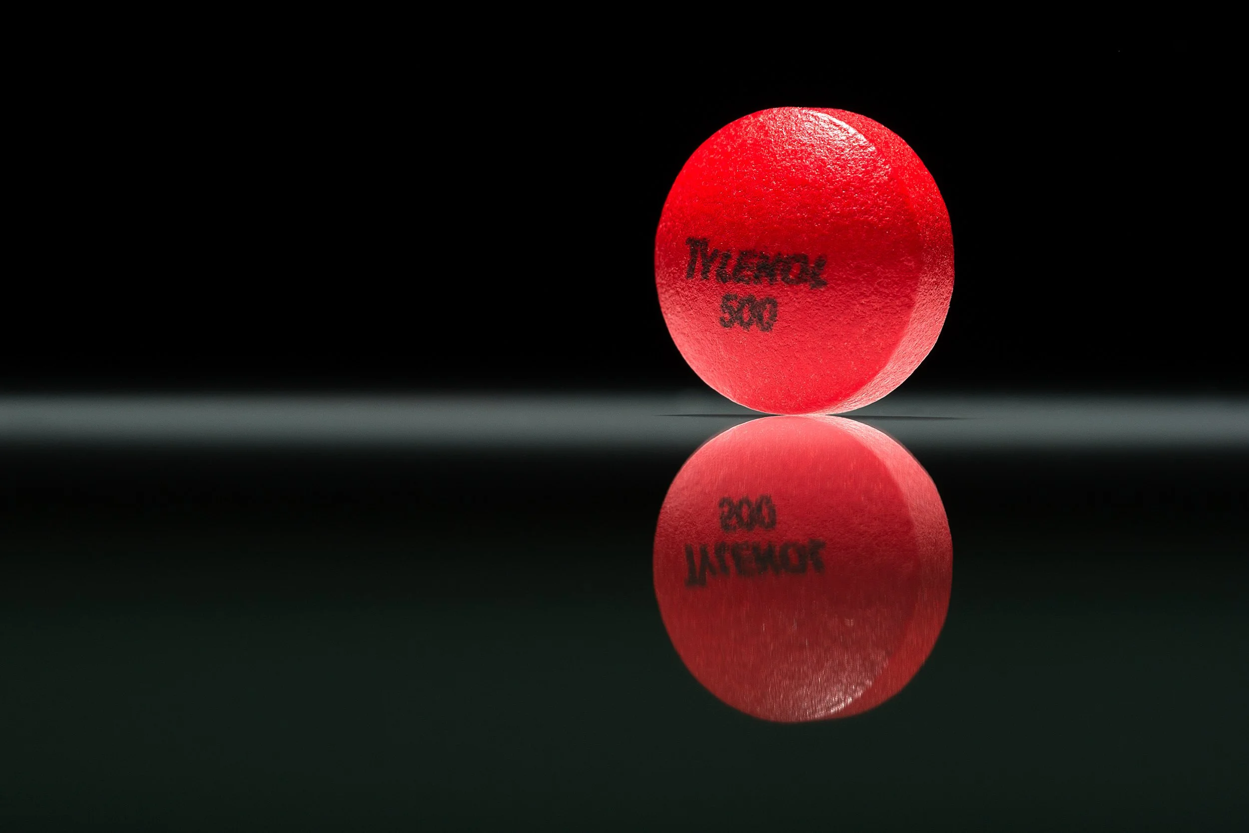 Single red Tylenol tablet with embossed label reflected on glossy surface