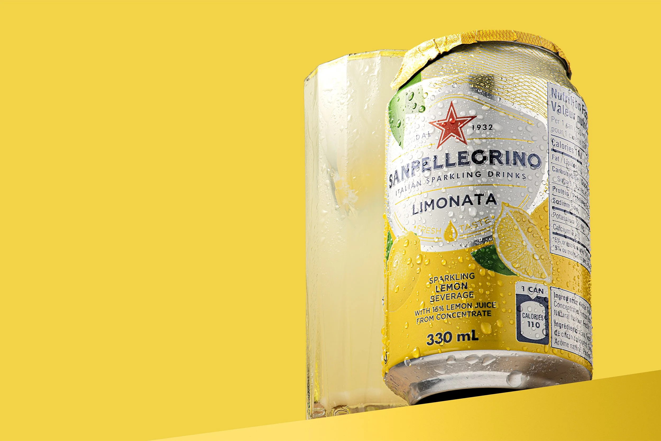 Sanpellegrino Limonata can with a cold glass of lemon drink on yellow background