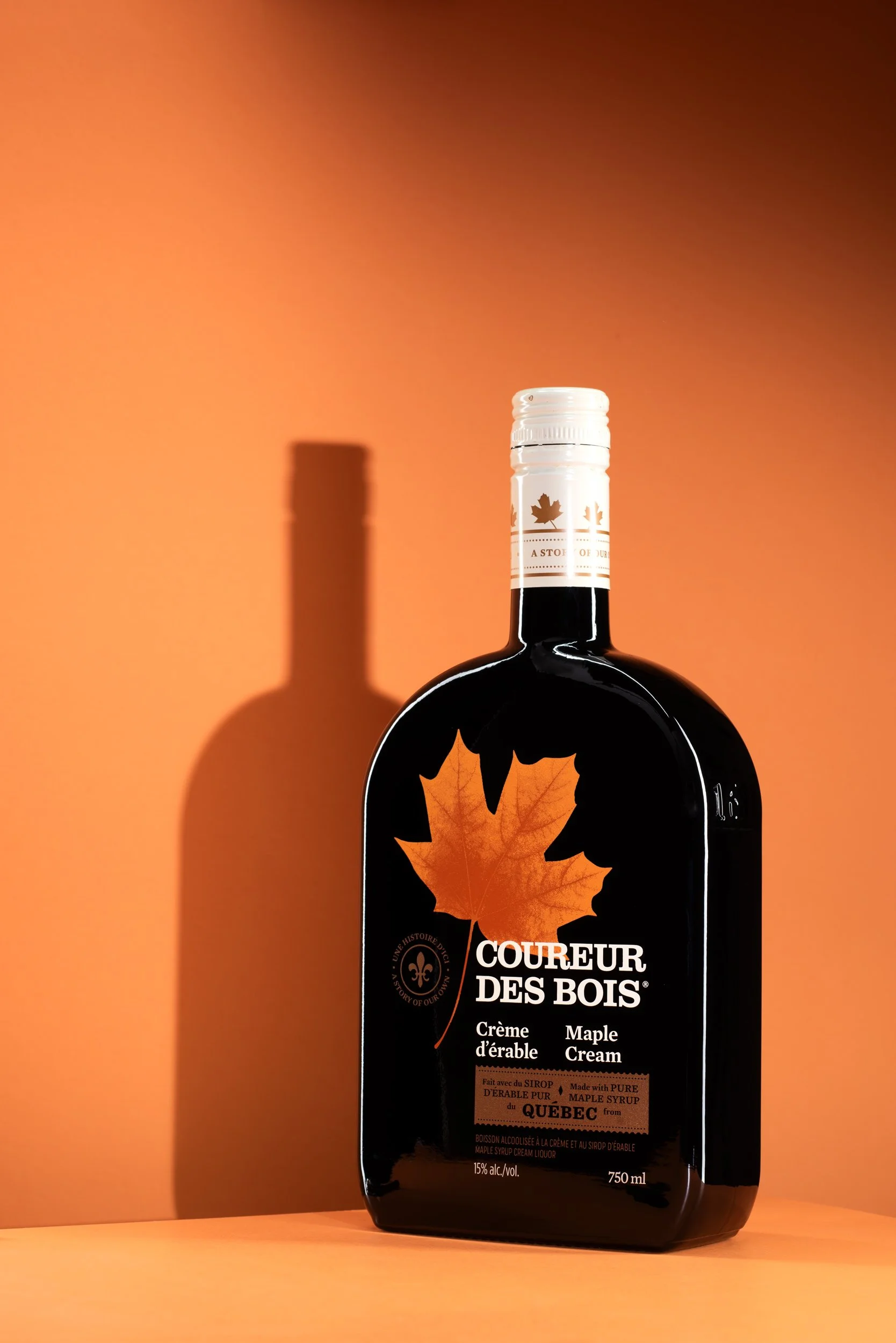 Coureur des Bois maple cream liqueur 750ml bottle on an orange background with a soft drop shadow beneath.