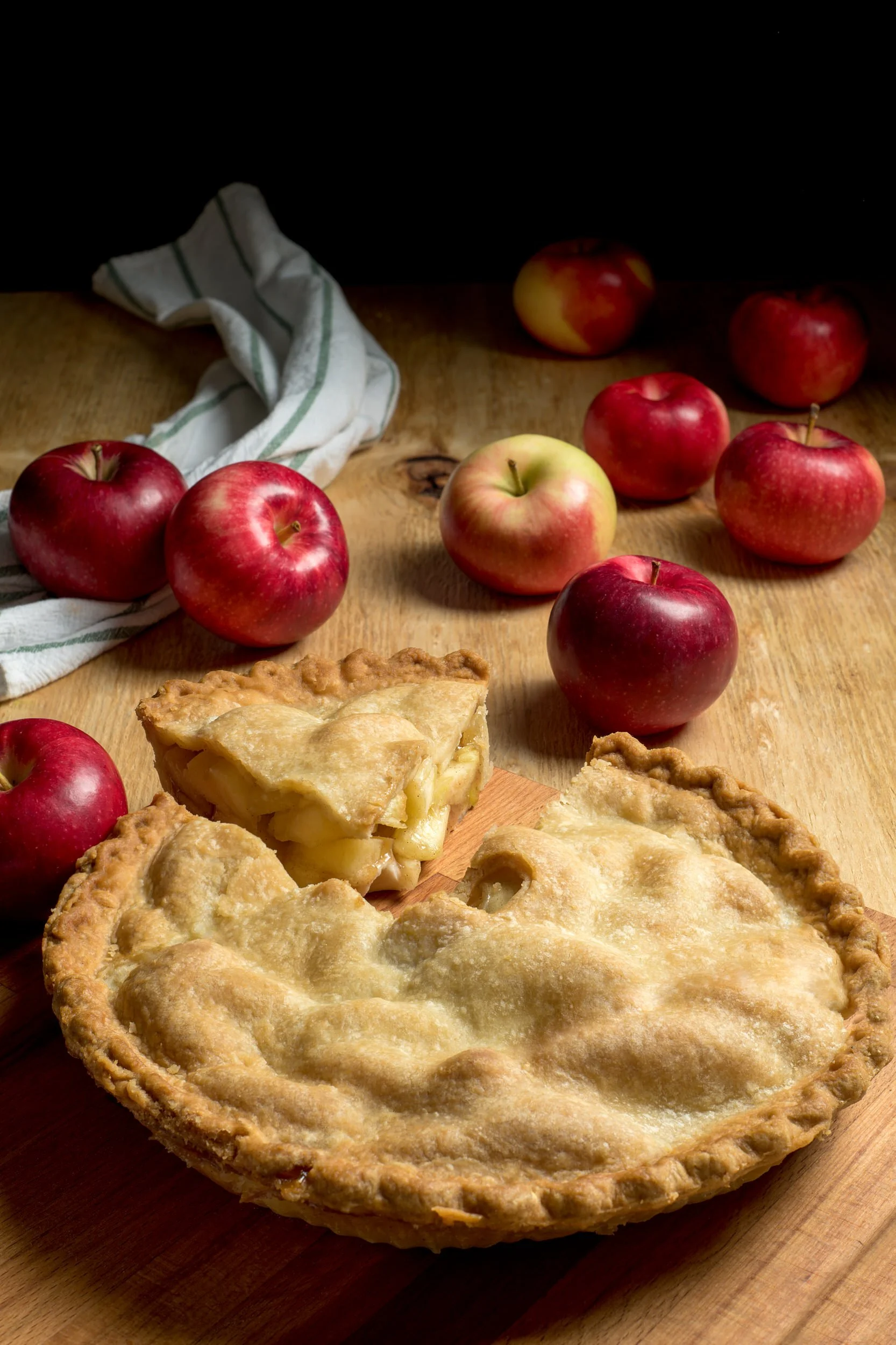 Sliced apple pie with golden crust surrounded by fresh apples