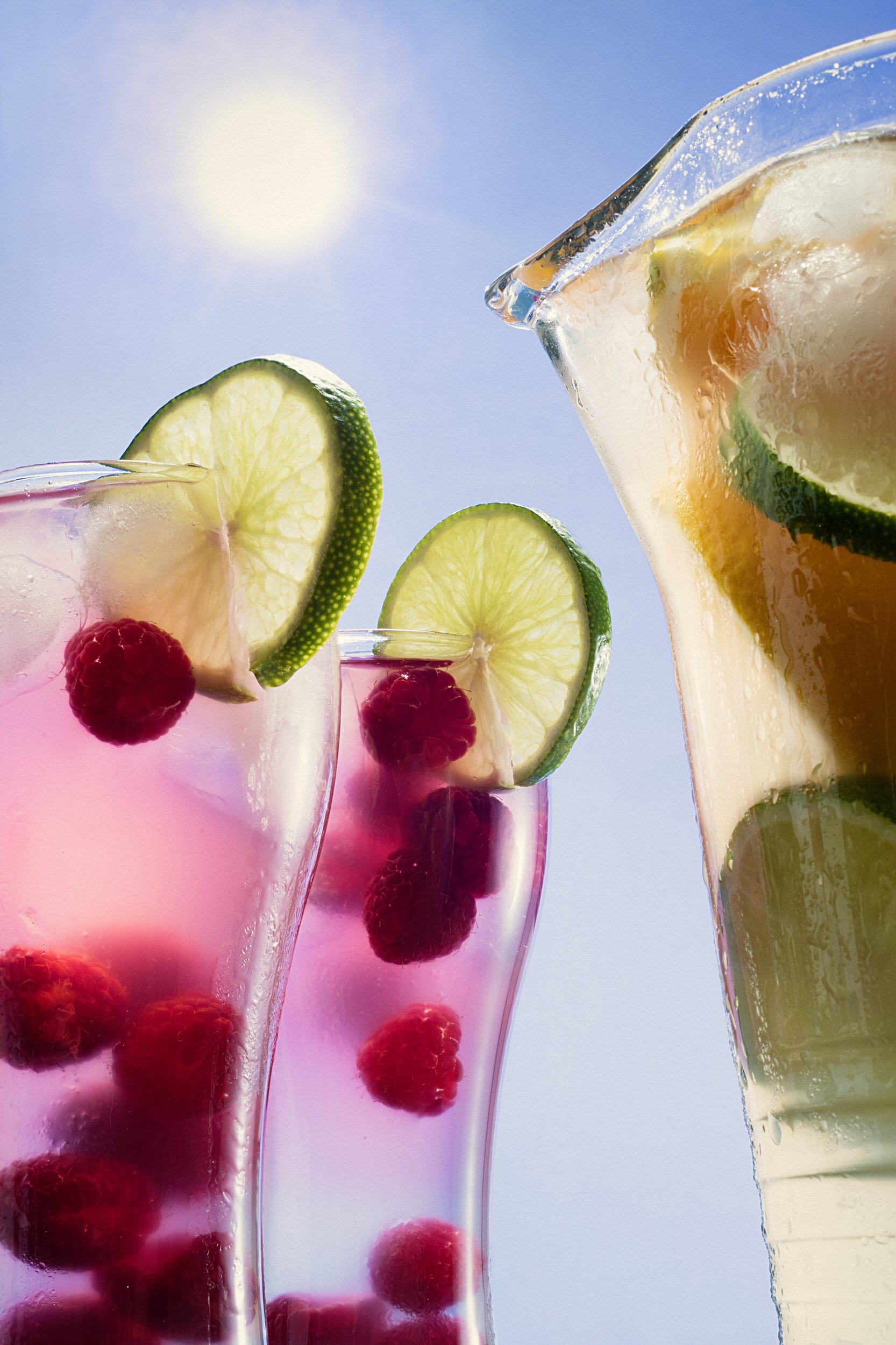Iced raspberry lime drinks in glasses and a pitcher under bright sunlight