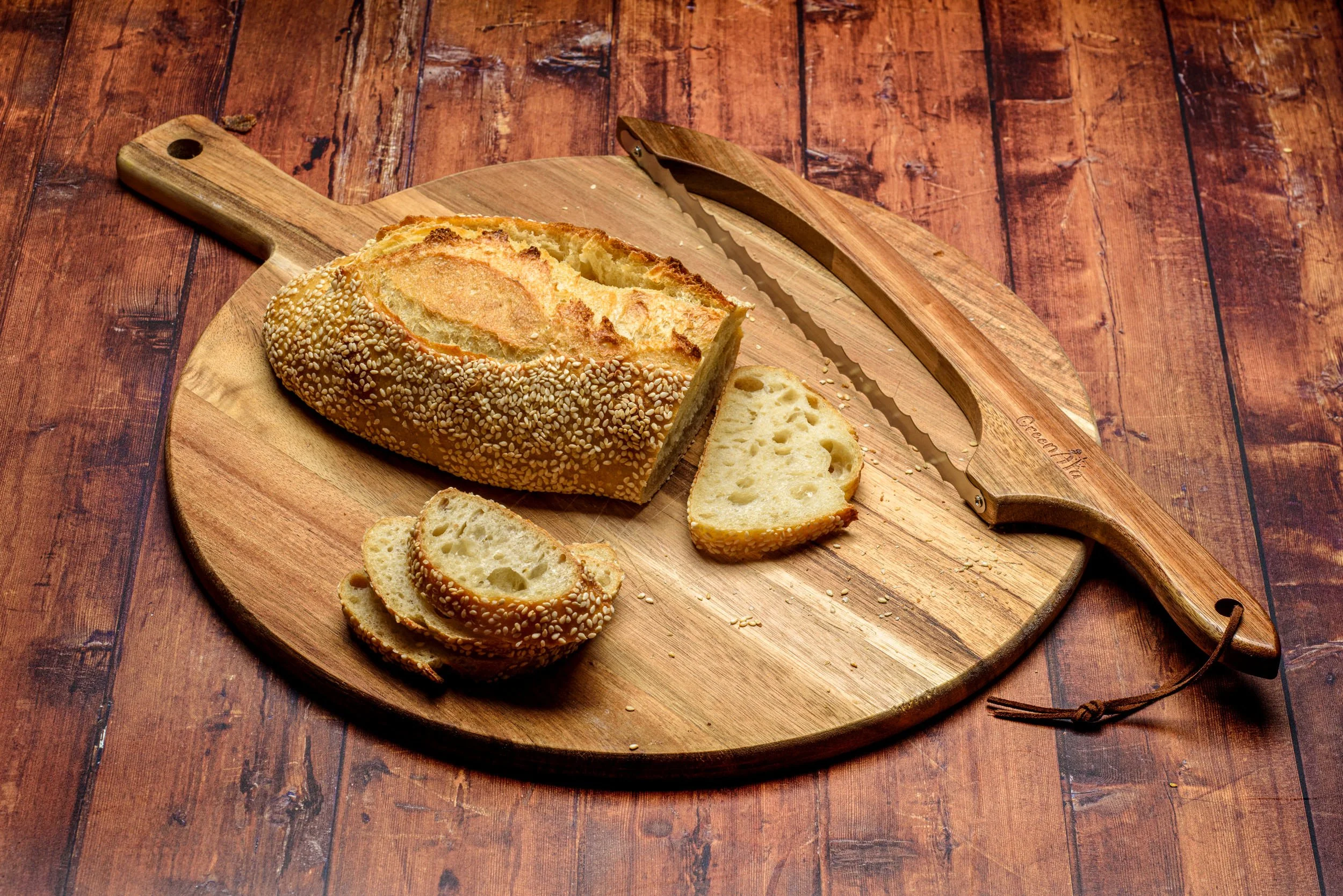Green Ara knife beside a sesame loaf and slices on a round cutting board