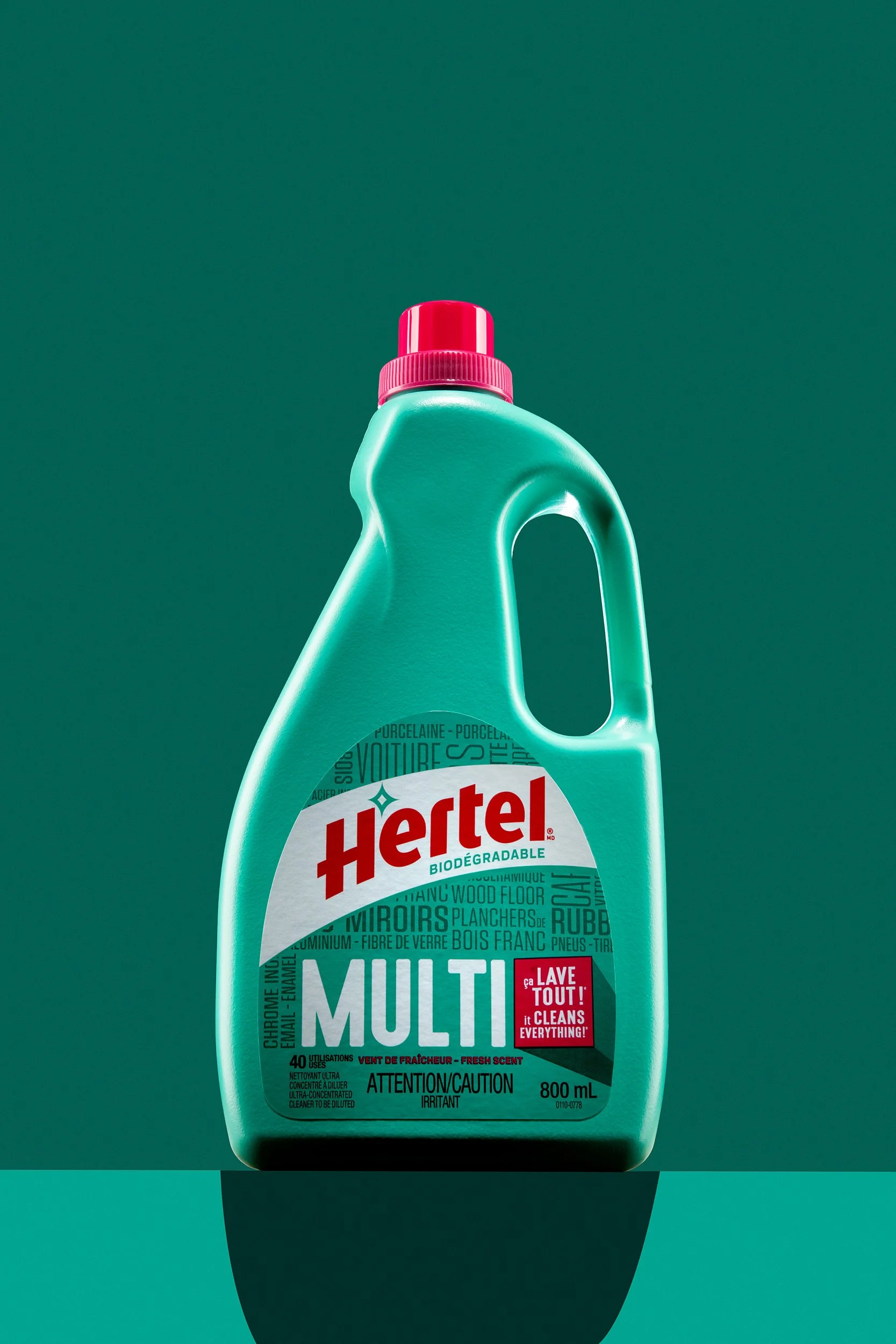Green bottle of Hertel Multi cleaner with red cap centered on teal background