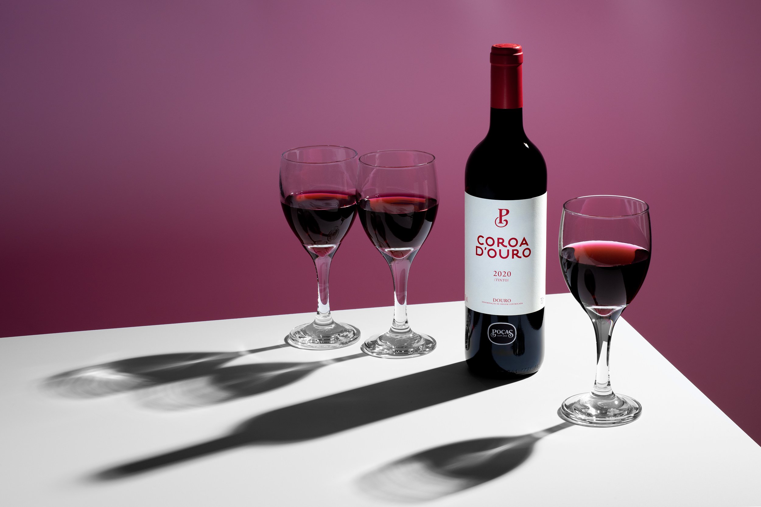 Bottle of Coroa d'Oro red wine and glasses on a magenta background with sharp shadows, beverage photographer Montreal 