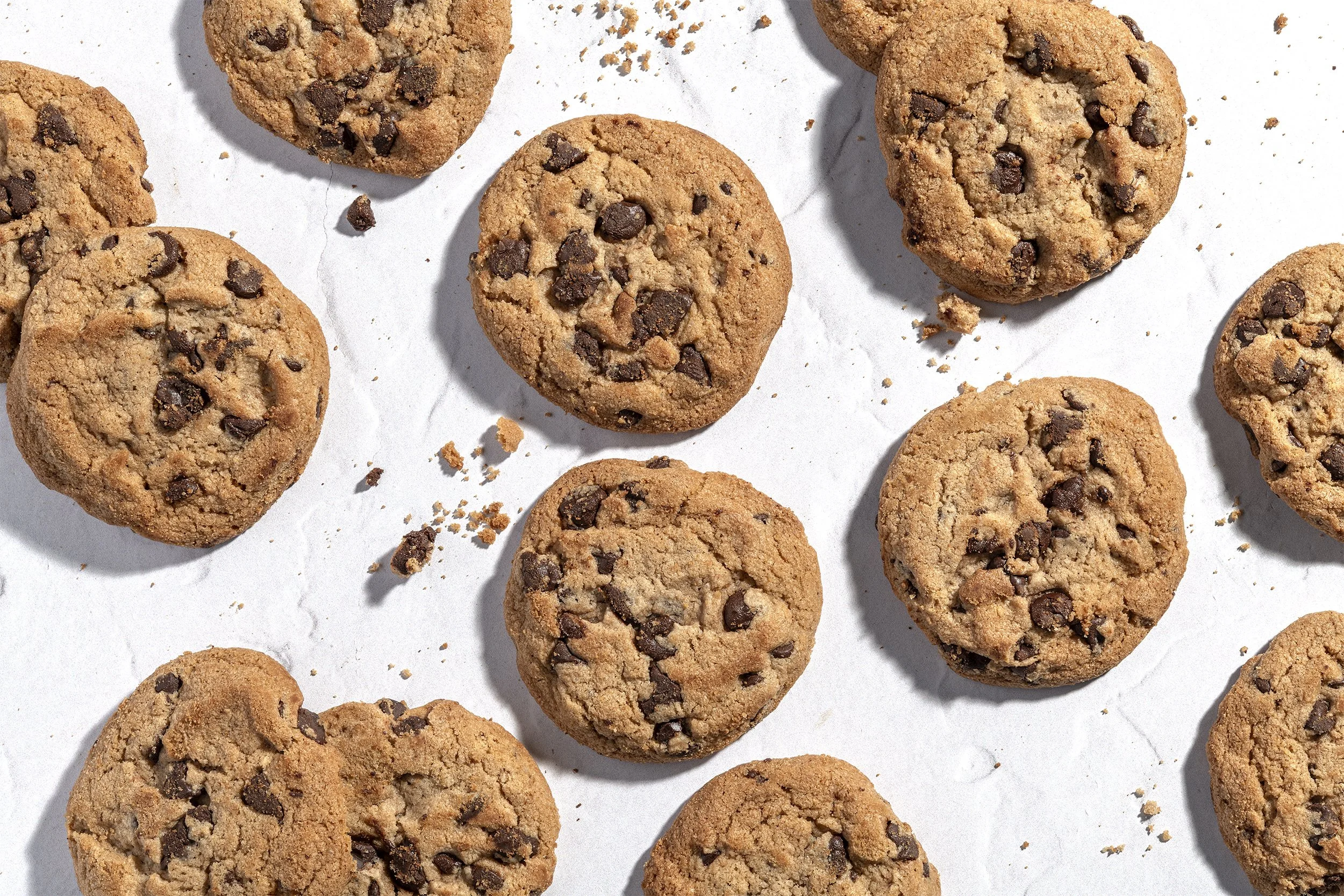 Flat lay of multiple chocolate chip cookies with crumbs on white background