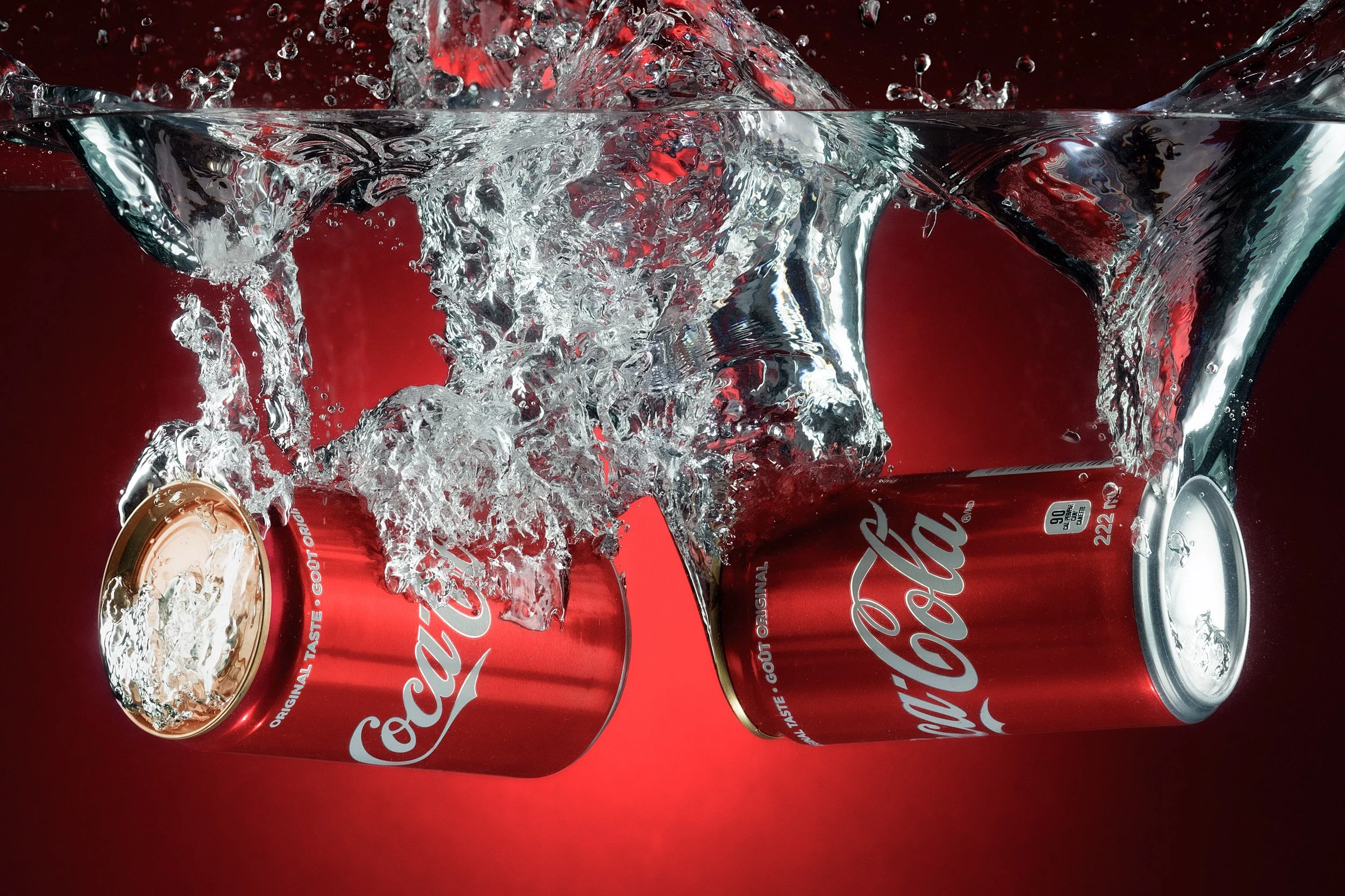 Coca Cola cans falling into water with splash effect on red background