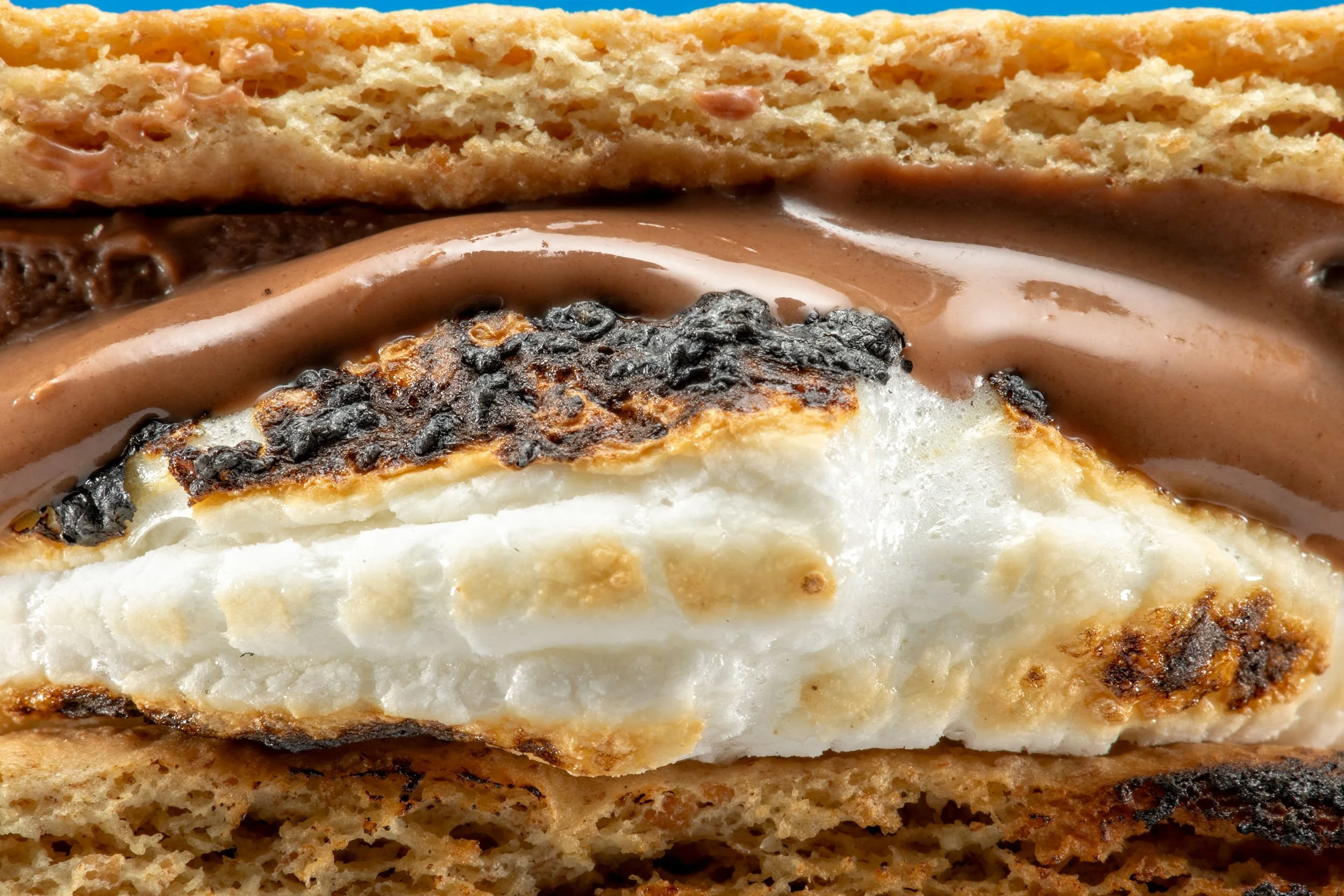 Extreme close-up of a s’more showing gooey chocolate and charred marshmallow between graham crackers