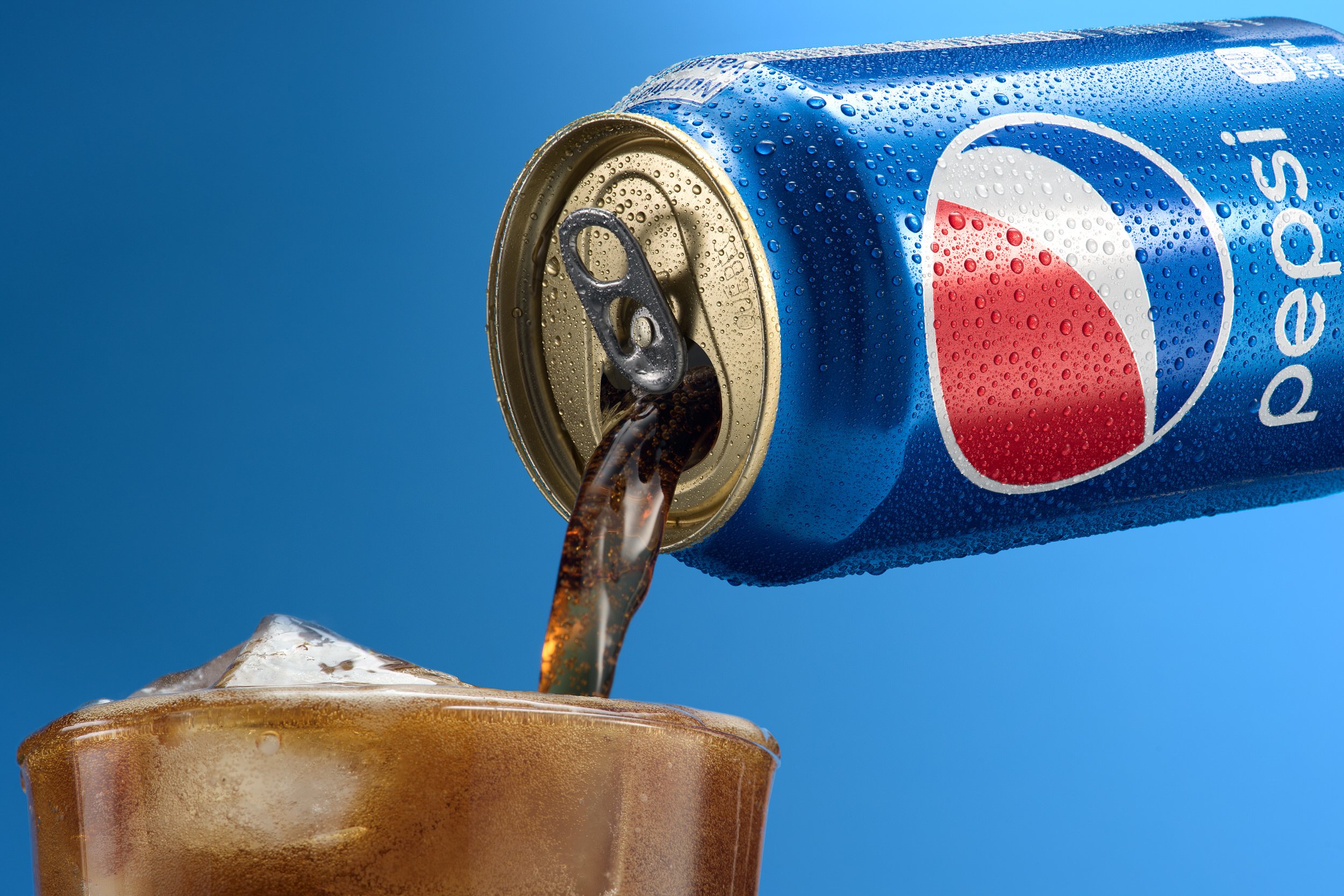 Close-up of a cold Pepsi can pouring cola into a glass filled with ice