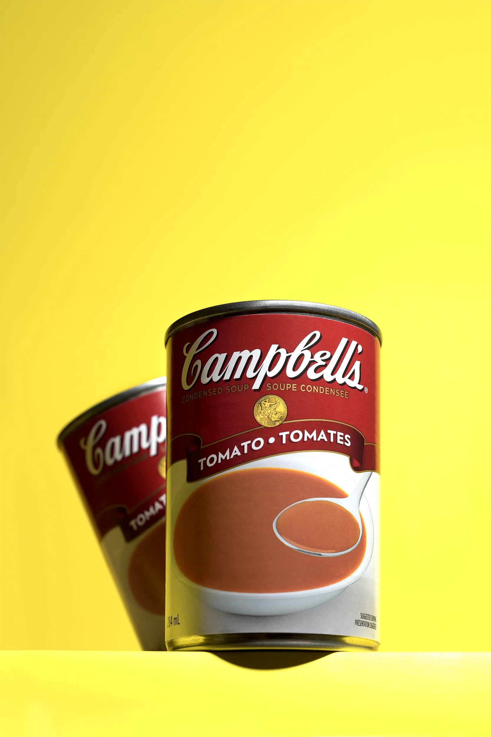 Campbells red soup can in foreground with second can behind on yellow