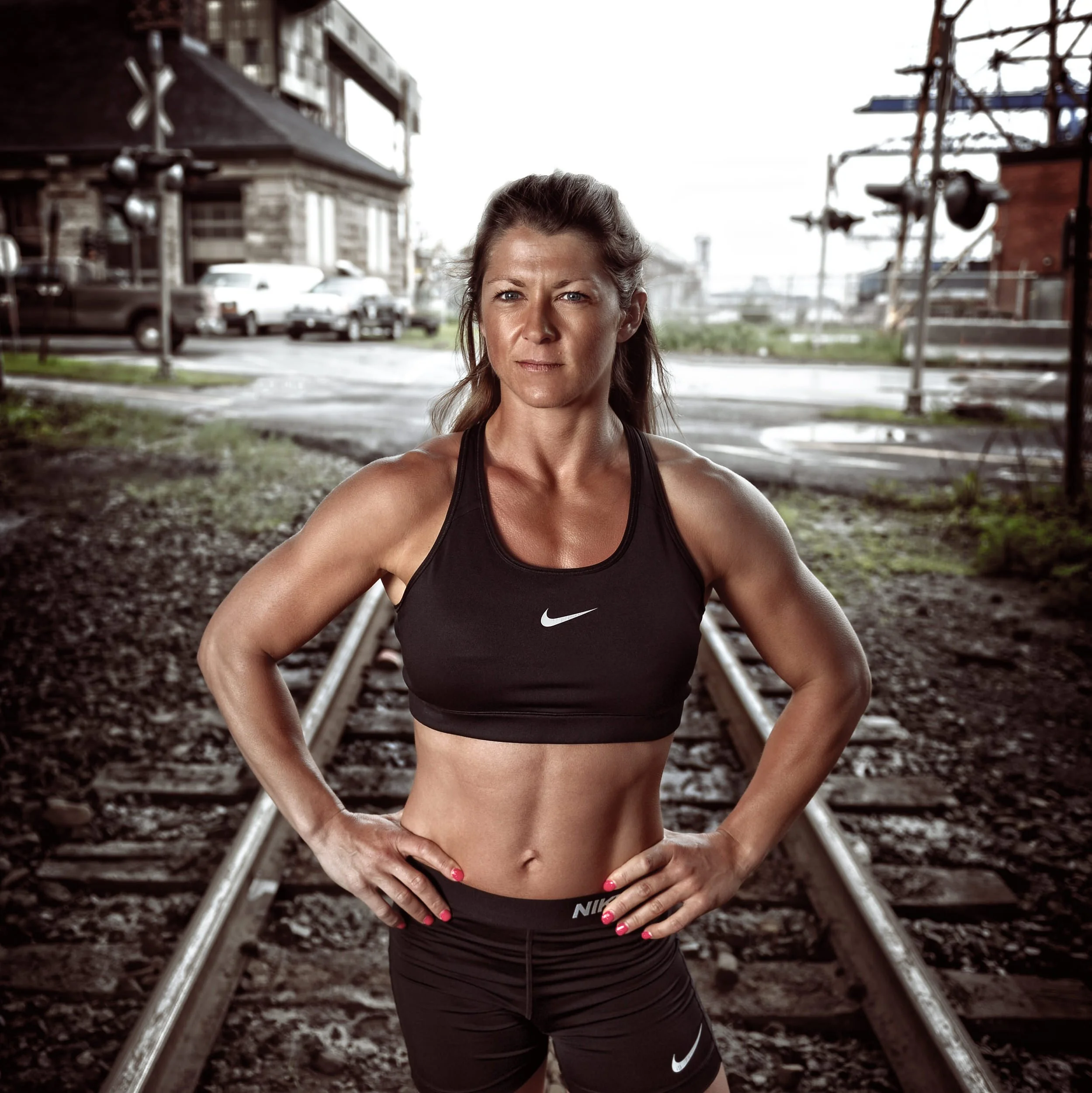 Strong woman in sportswear posing with hands on hips on train tracks