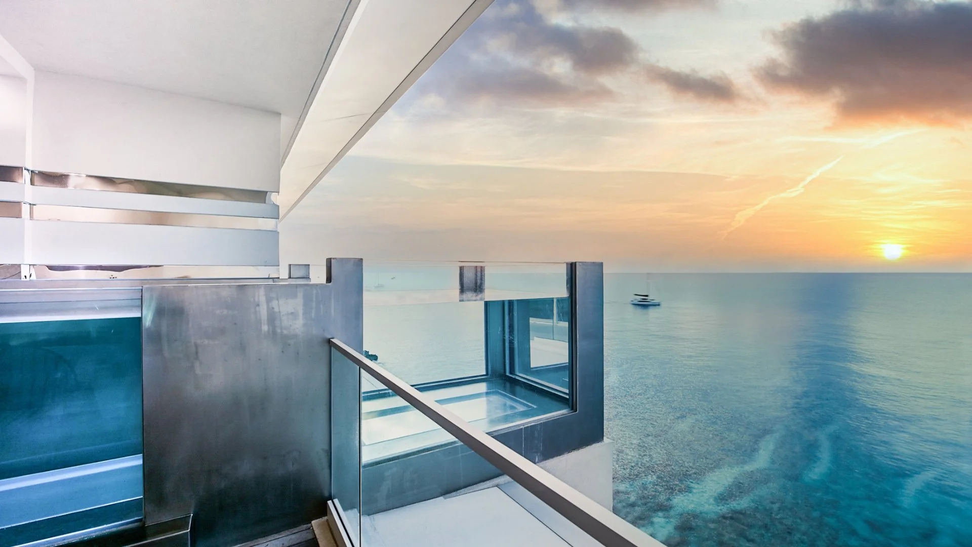 Alt Text: Ocean view from a modern balcony featuring a glass railing and an integrated glass plunge pool during a vibrant tropical sunset.