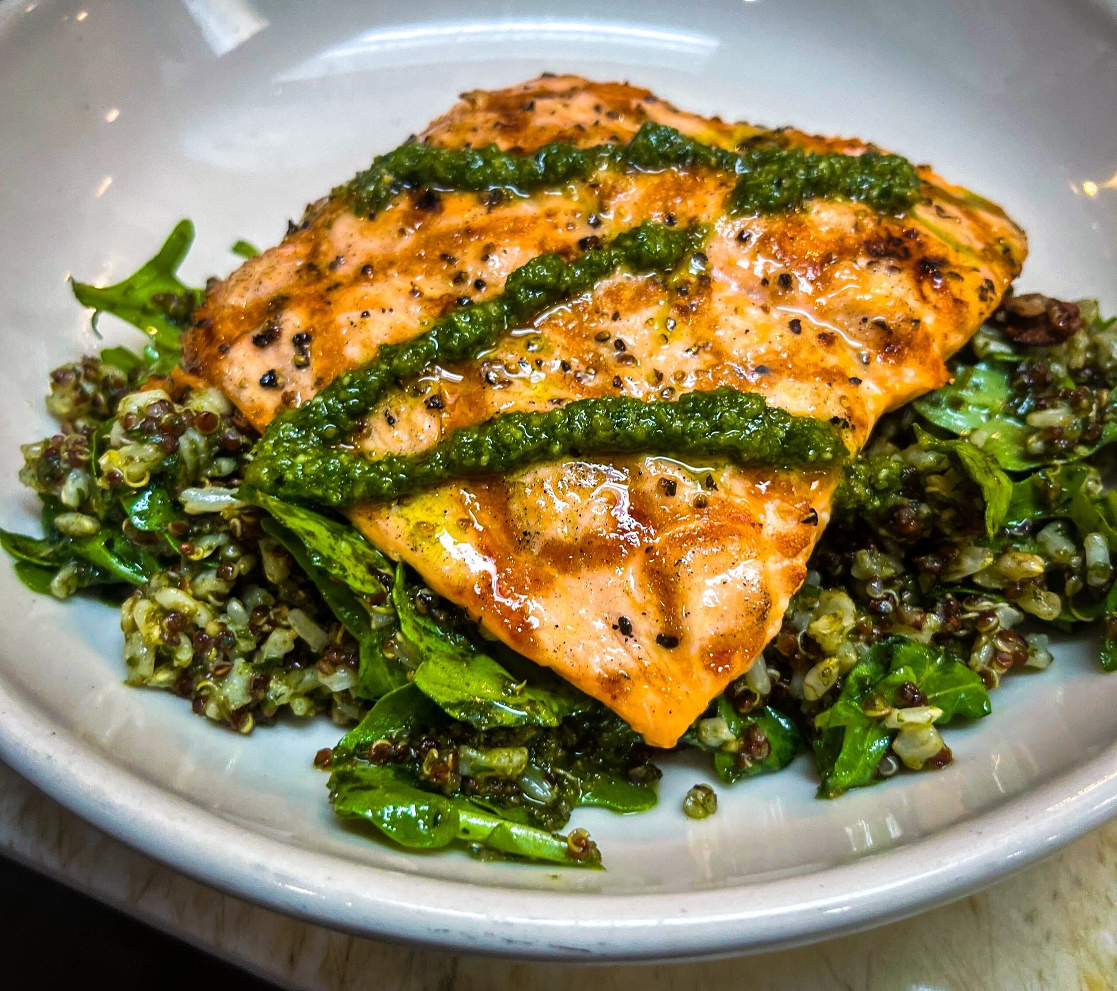 Enjoy a deliciously wholesome bite in every forkful! 💚 Our salmon is grilled to perfection and served over a savory blend of quinoa, brown rice, and arugula and finished with our fabulous homemade pumpkin seed pesto. 
.
.
.
#homemadepesto #pestosalm