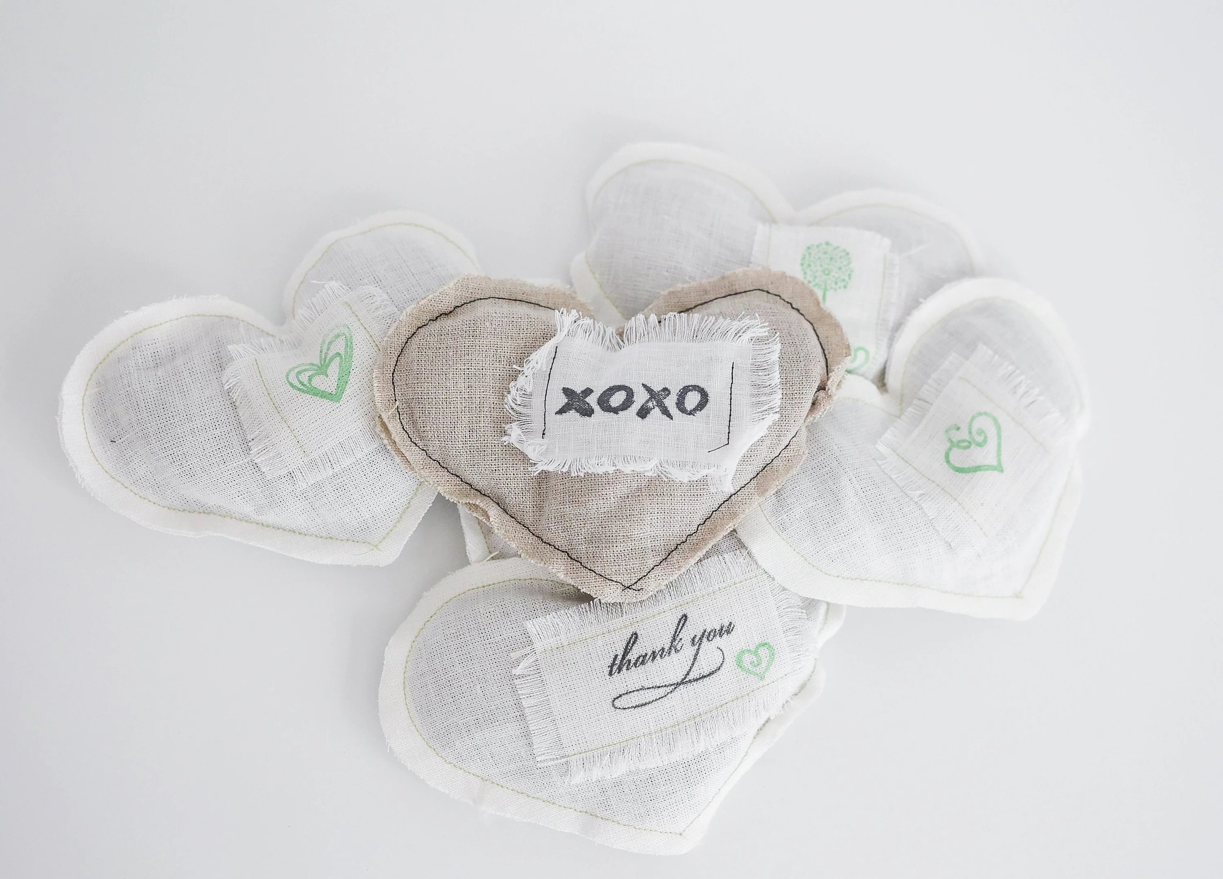 Collection of fabric hearts with embroidered and printed messages, including one with 'XOXO' and another with 'thank you', on a white background.
