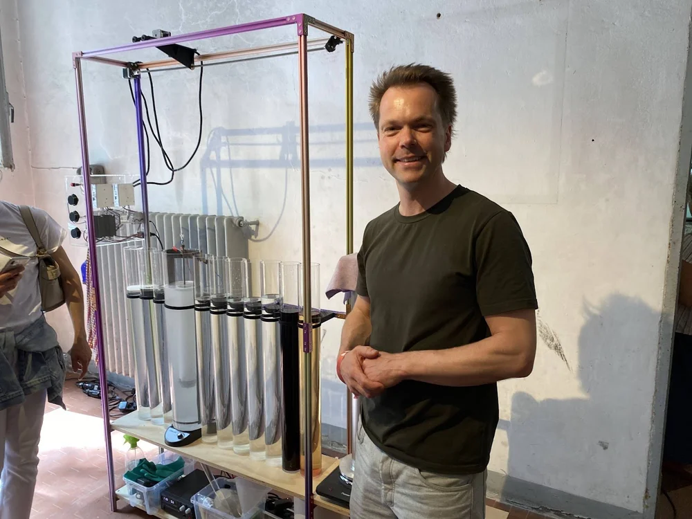 Image of man standing in front of series of clear cylinders filled with liquid 