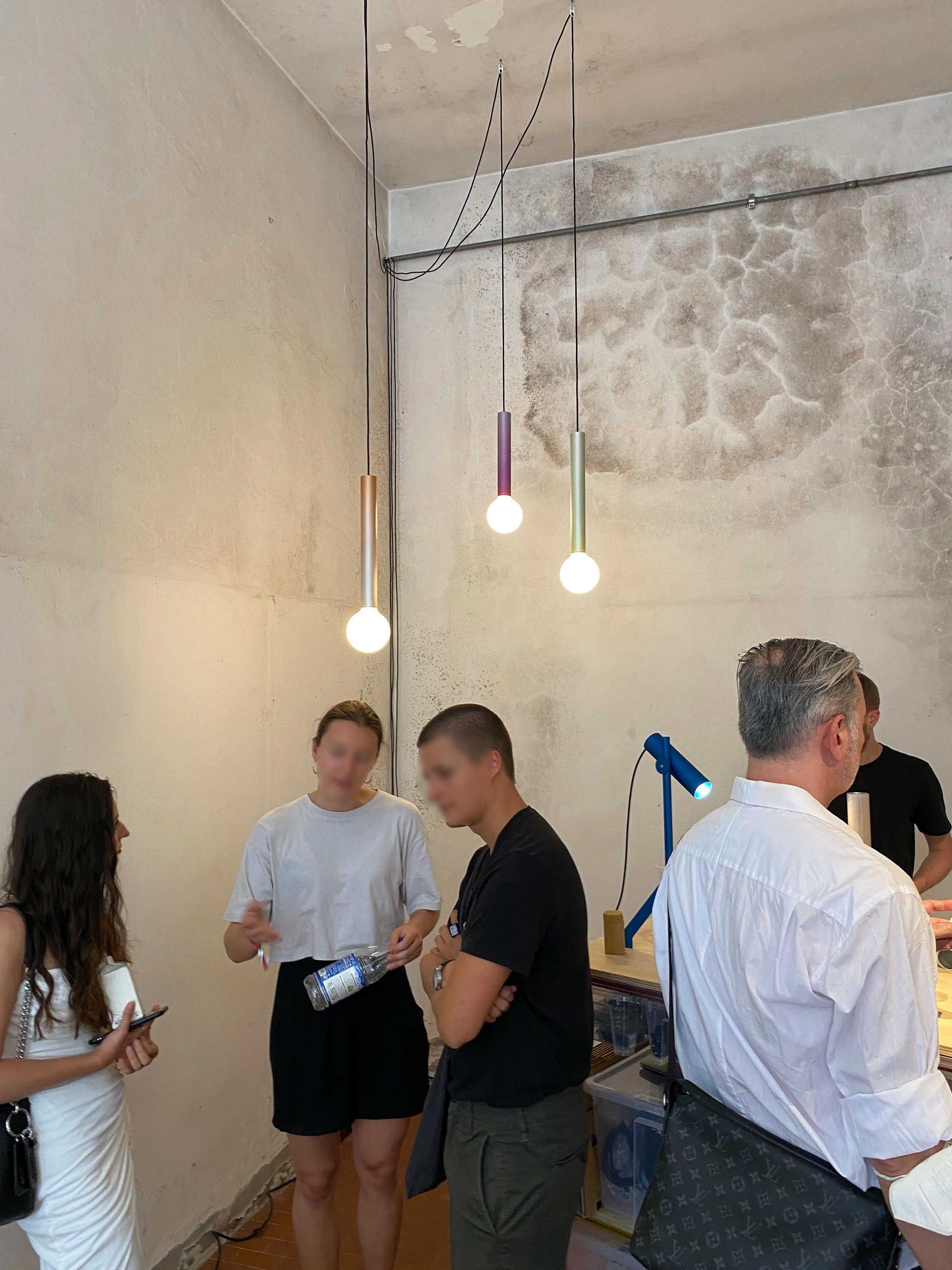 Image of three lights hanging from ceiling and a blue lamp on a table with people in foreground 
