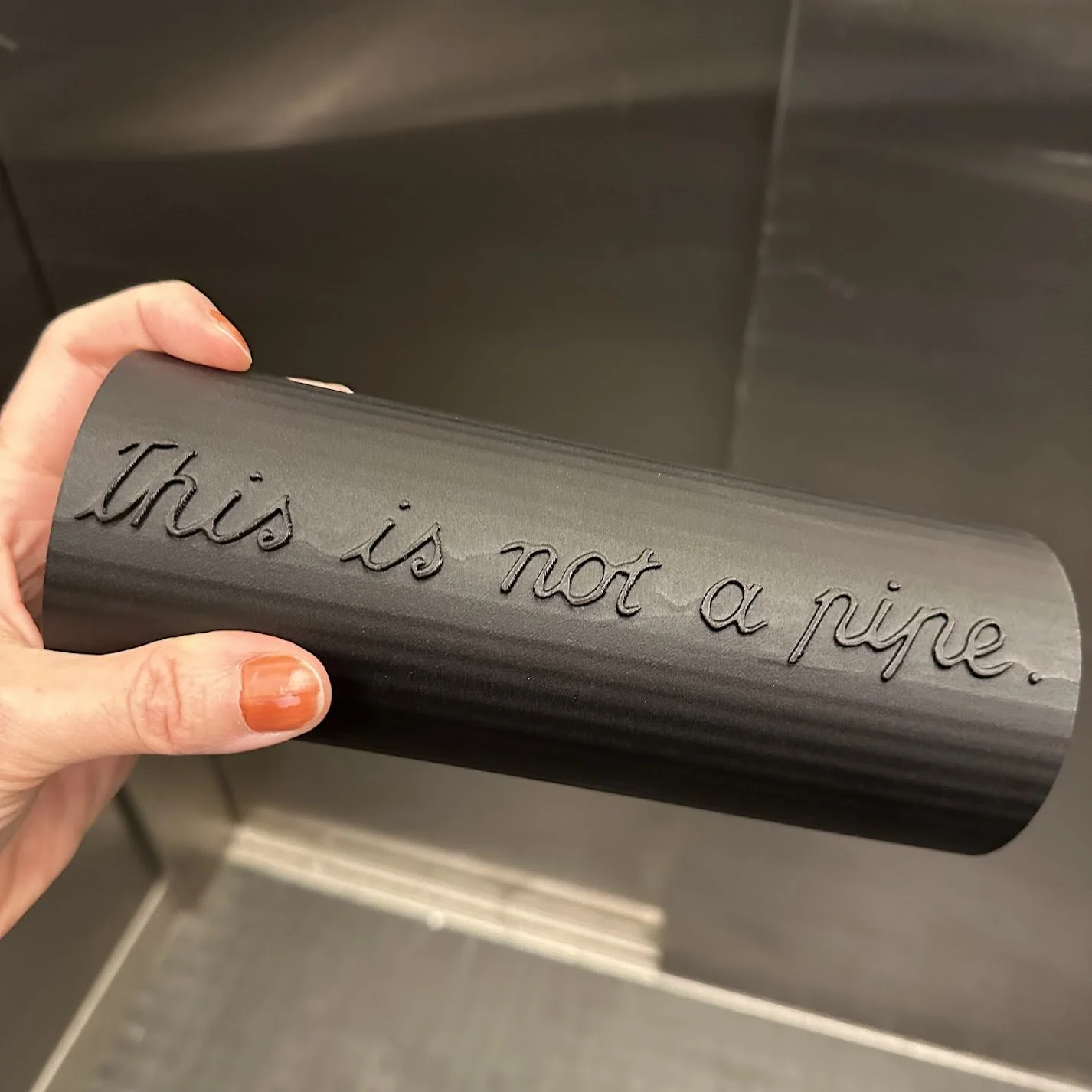 A hand holding a black cylindrical tube with the text This is Not a Pipe