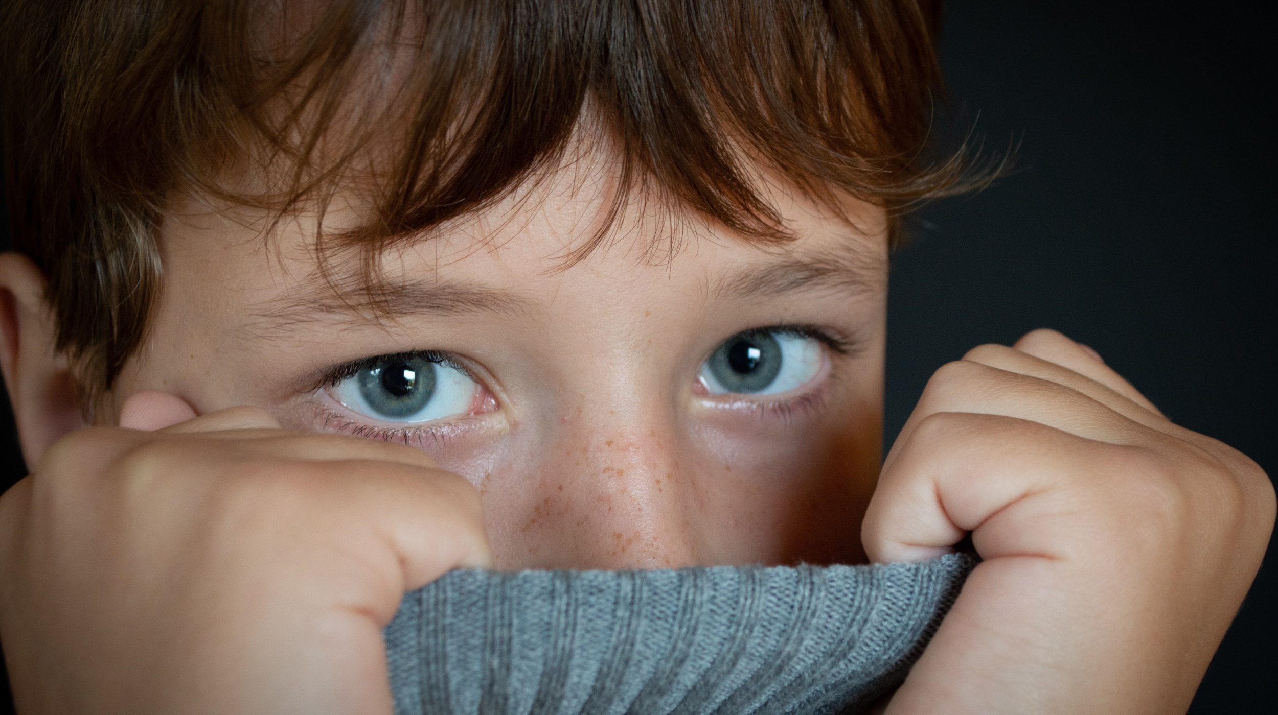 Masking Isn’t a Superpower: What Camouflaging Really Costs Autistic Kids (and Teens). young boy with brown hair and blue eyes holding shirt over his mouth and nose looking at the camera. masking.