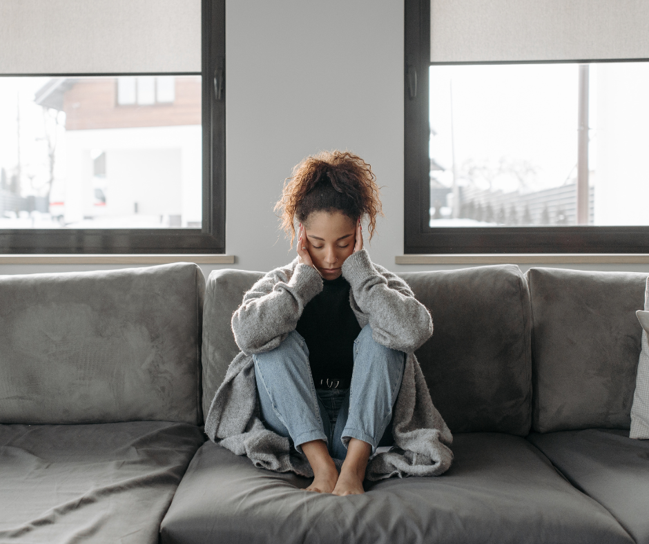 A woman sitting on a couch and feeling overwhelmed.