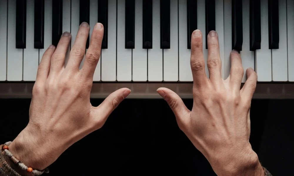 Two hands poised over piano keys, suggesting the start of a musical piece. The focus is on fingers ready to play, creating a mood of anticipation and artistry.