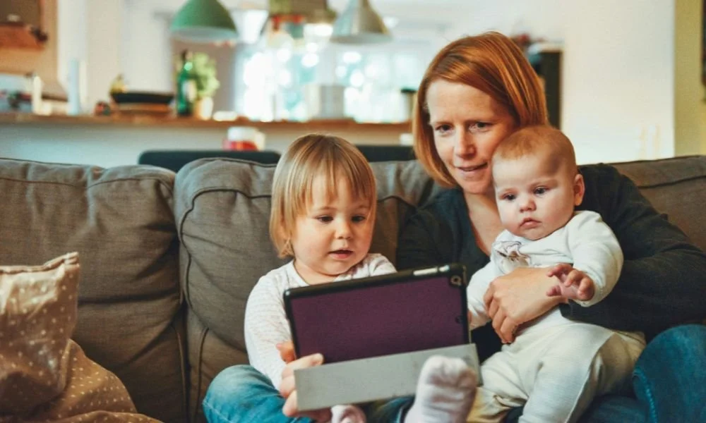two-babies-and-woman-sitting-on-sofa-while-holding-baby-and-watching-on-tablet