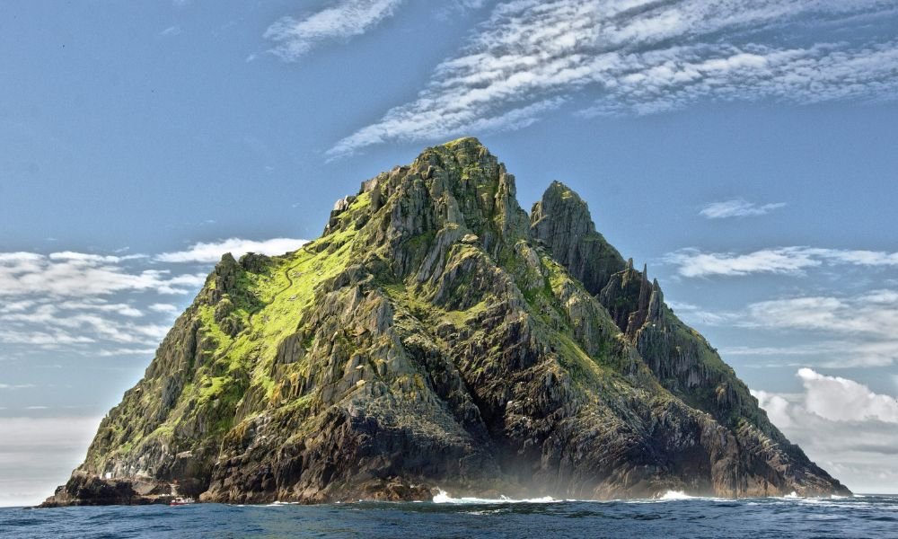 Steep rocky island with lush green patches under a clear blue sky, surrounded by calm ocean waters, conveying a serene and majestic feel.
