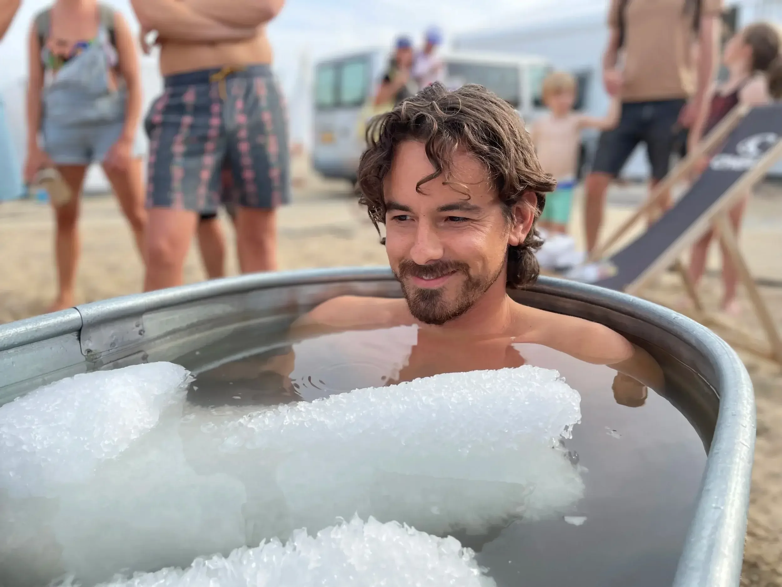 Man sitting in an ice bath outdoors with people in the background.