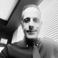 Black and white photo of a man with short hair, wearing a collared shirt, smiling slightly indoors.