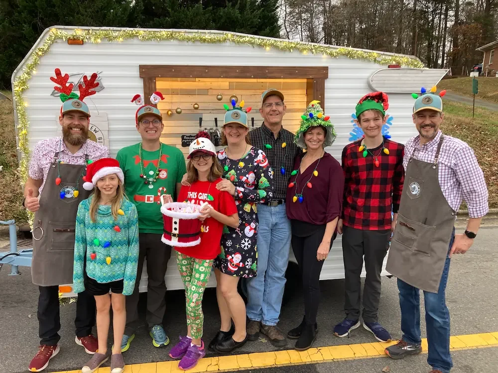 A group in holiday attire pose in front of the mobile tap trailer.