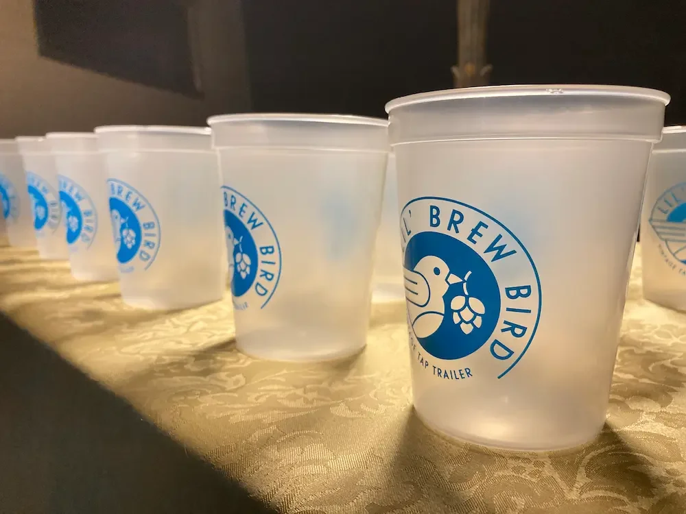 Translucent cups with Lil' Brew Bird logo are lit up at night. 