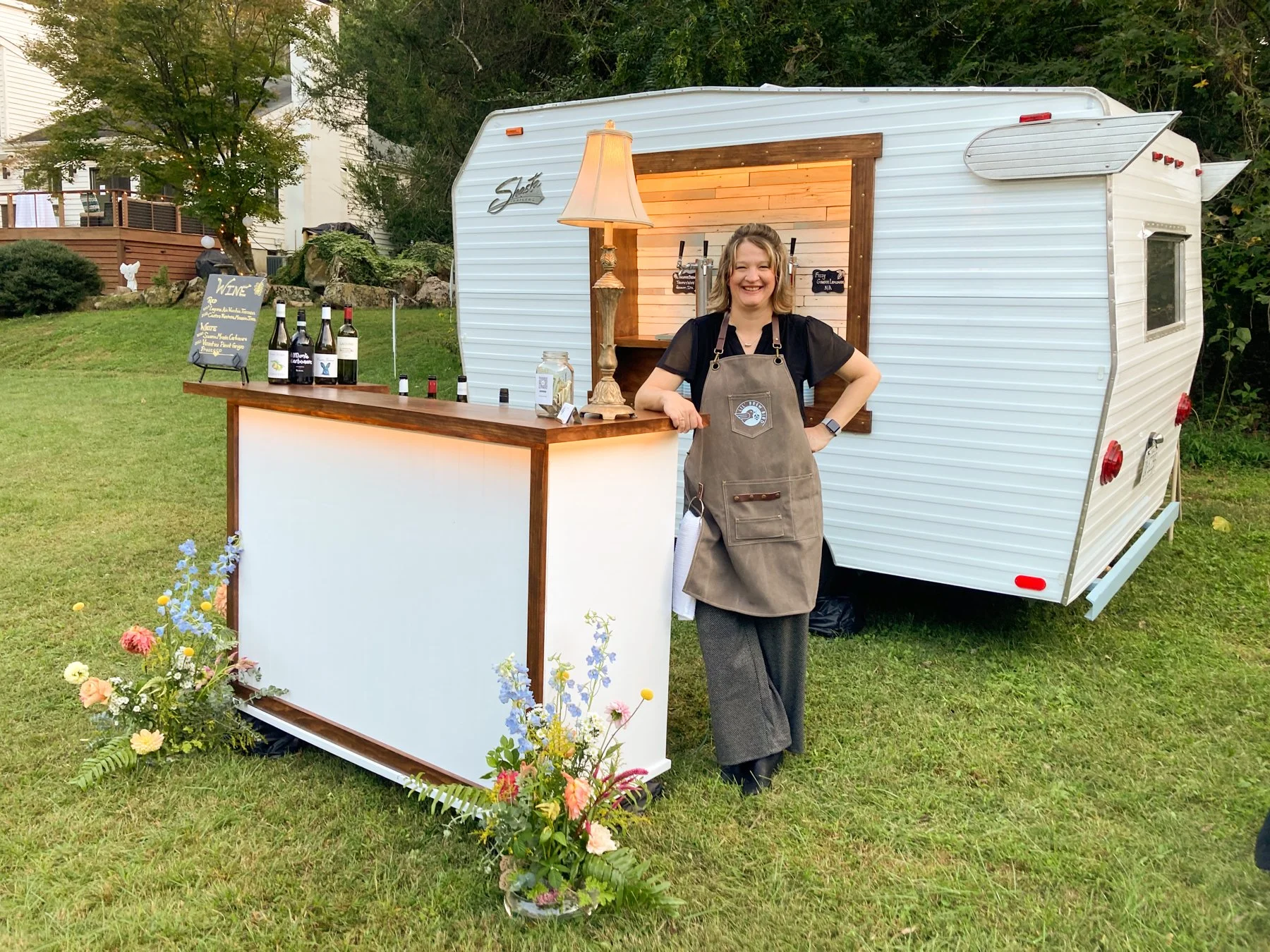 A bartender for Lil' Brew Bird stands alongside the portable bar all decorated with flowers for a wedding.
