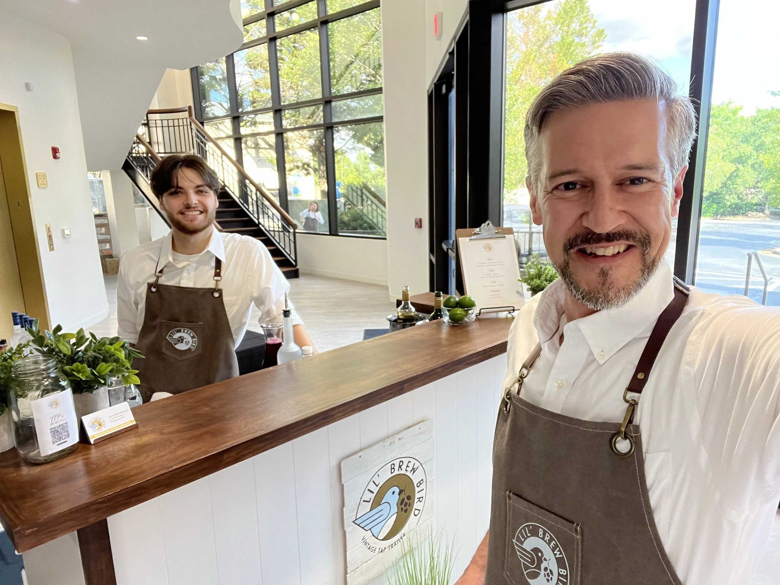 Two bartenders wearing aprons stand in front of a portable bar