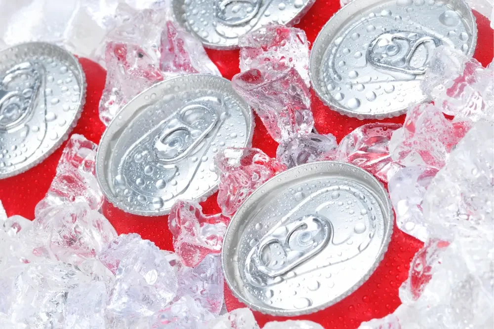 Close-up of soda cans with condensation, surrounded by ice cubes.