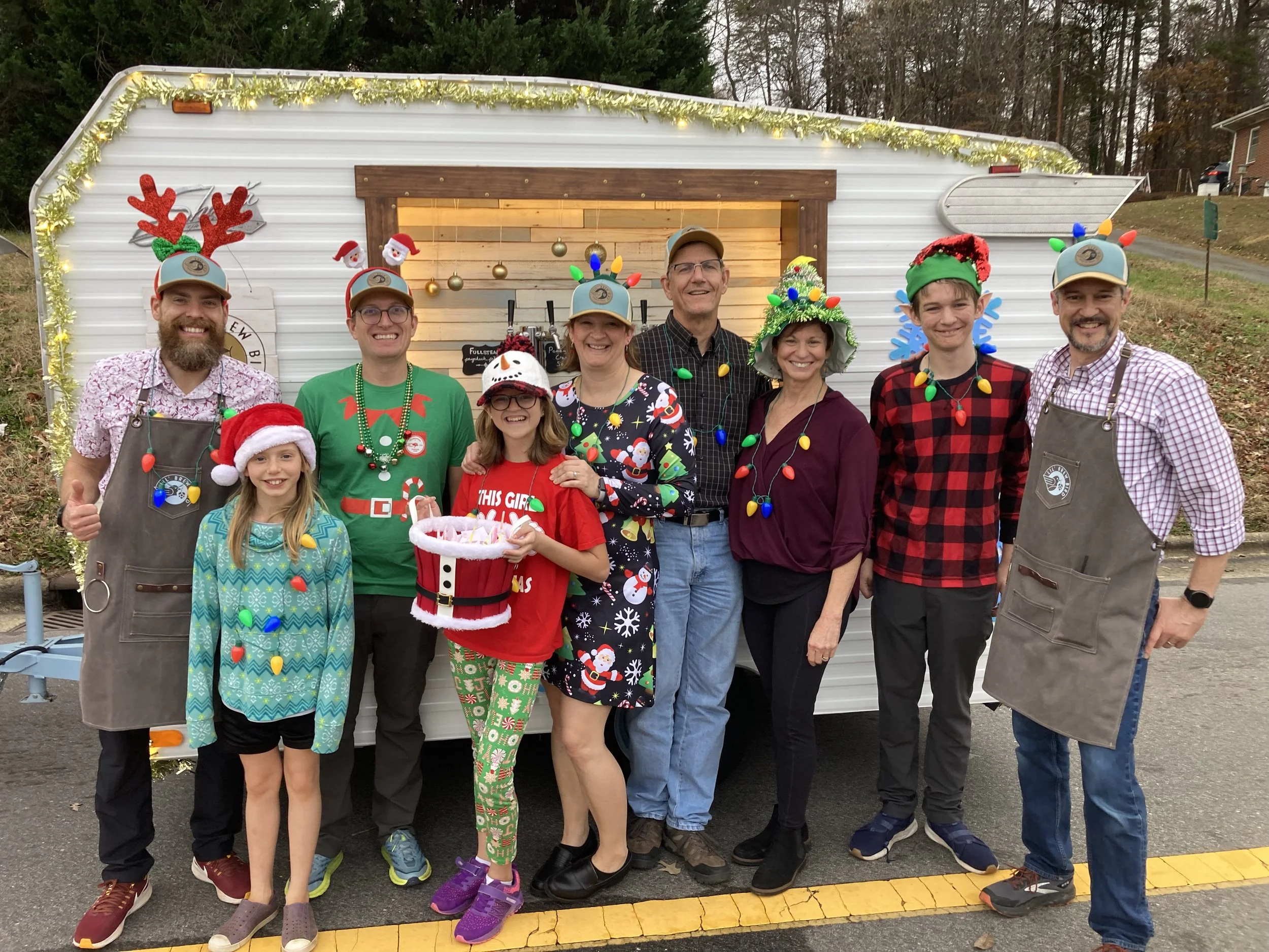 A group in holiday attire pose in front of the mobile tap trailer.