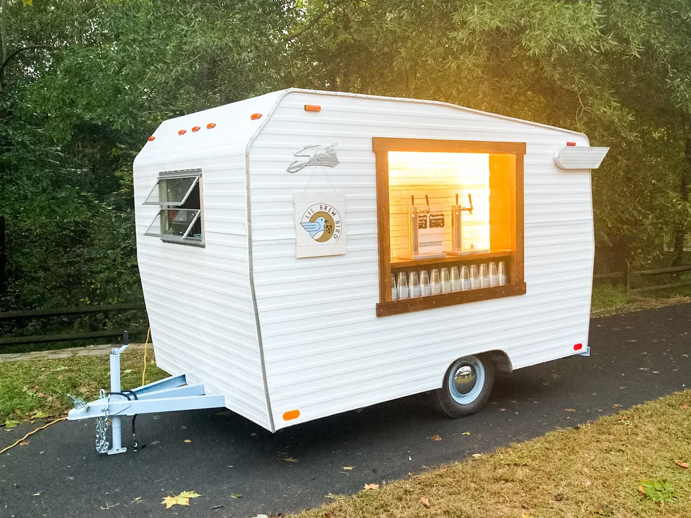 The vintage tap trailer, surrounded by trees and parked on a paved surface at dawn.